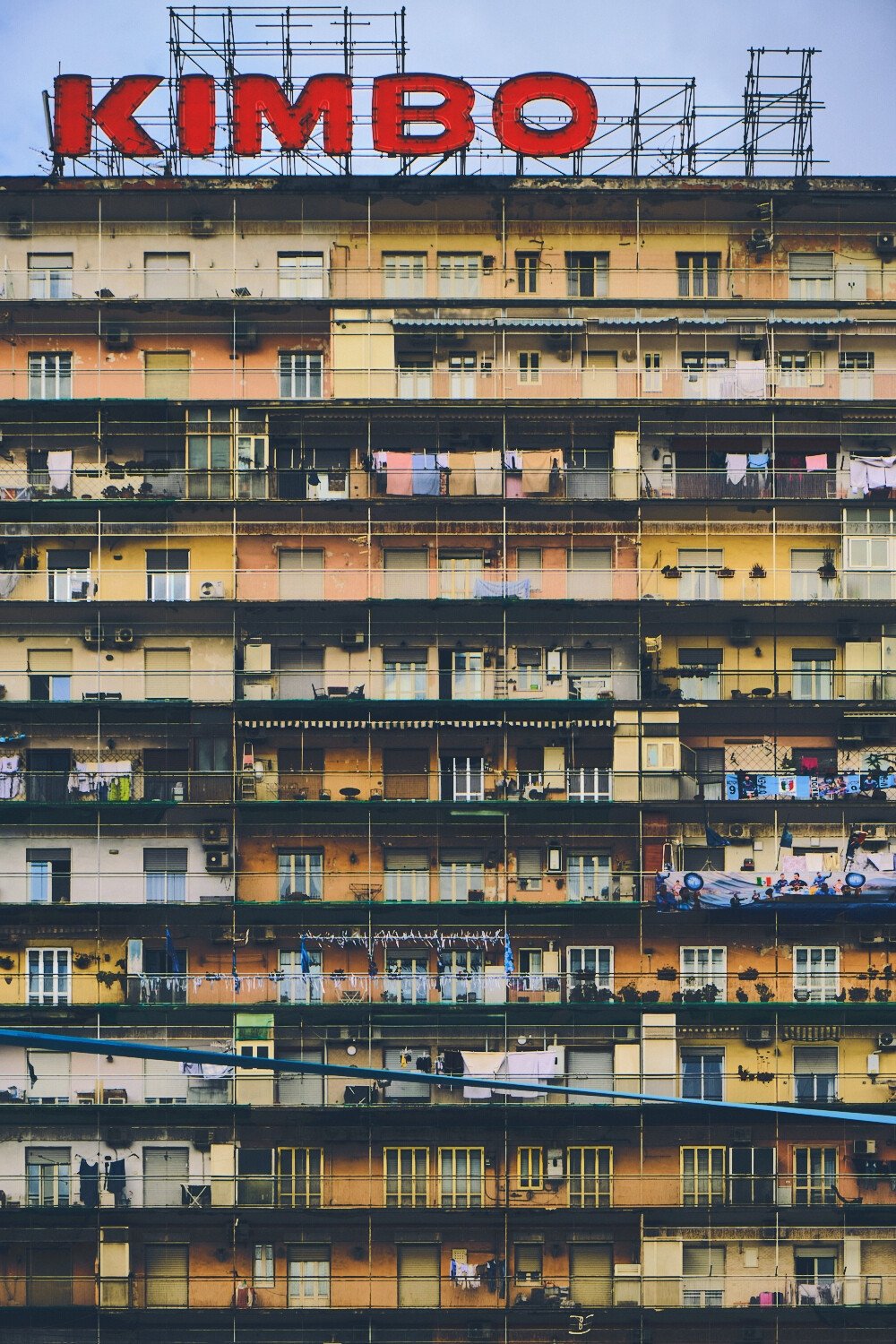 Multi-story residential building with laundry hanging from balconies and a large red sign on the roof spelling 'KIMBO'