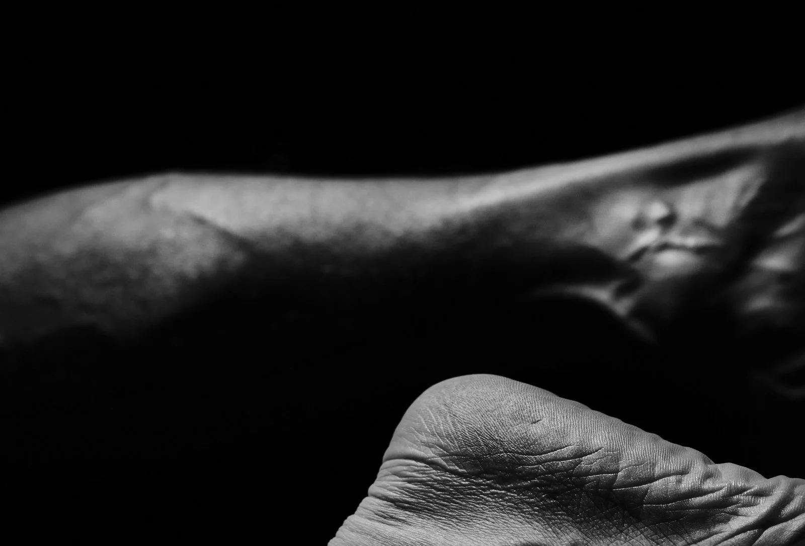 Close-up of a person's hand with visible wrinkles, holding an object in a dark environment with low lighting.