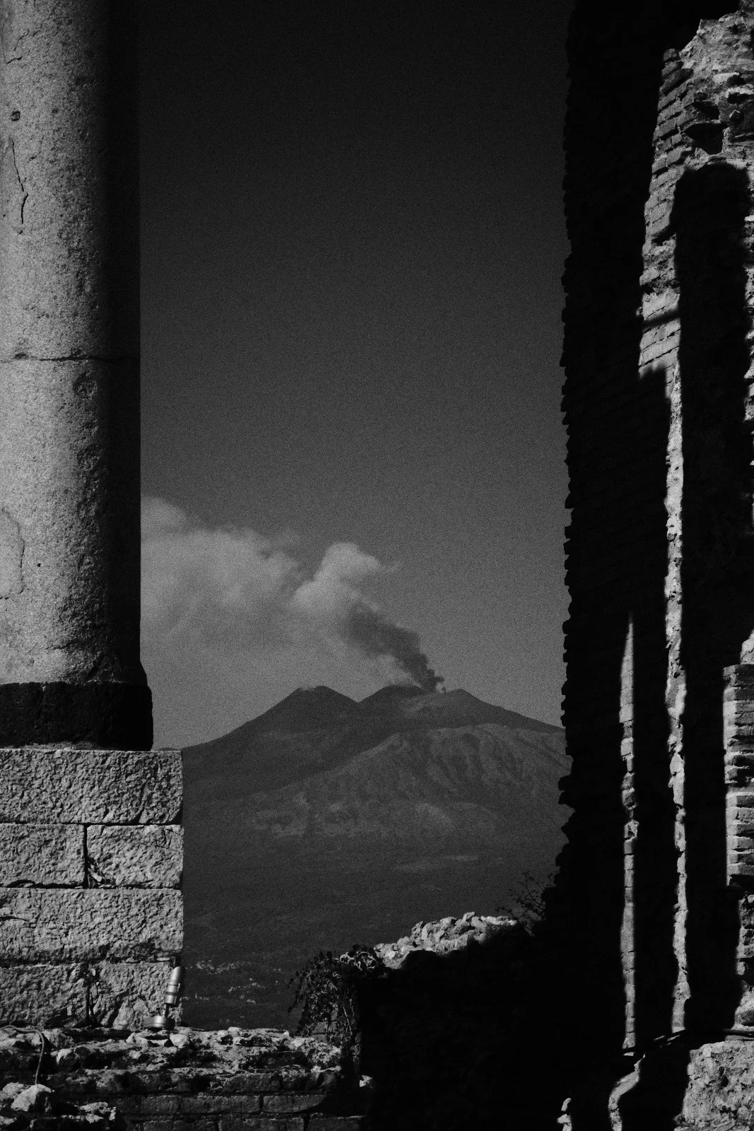 Ancient column and brick ruins framing Mount Etna with an ash plume rising from the crater, Taormina — Whispers of Form by Tom Imio