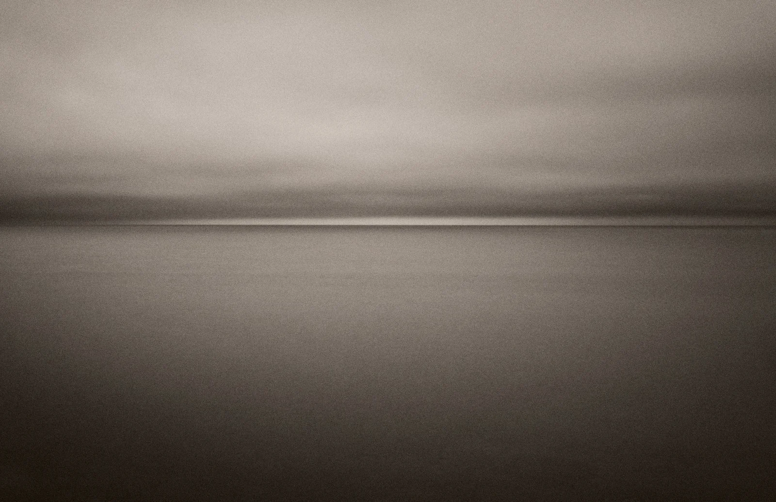 Minimalist long exposure seascape with a thin line of light on the horizon in sepia tones — Mare Incognitum by Tom Imio