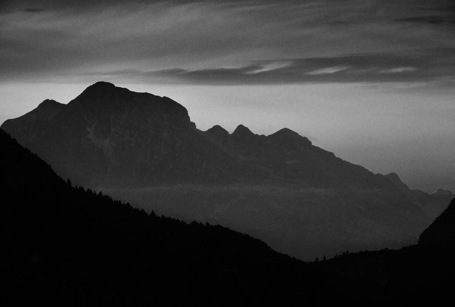 Black and white photo of a mountain range with layered ridges and clouds overhead.
