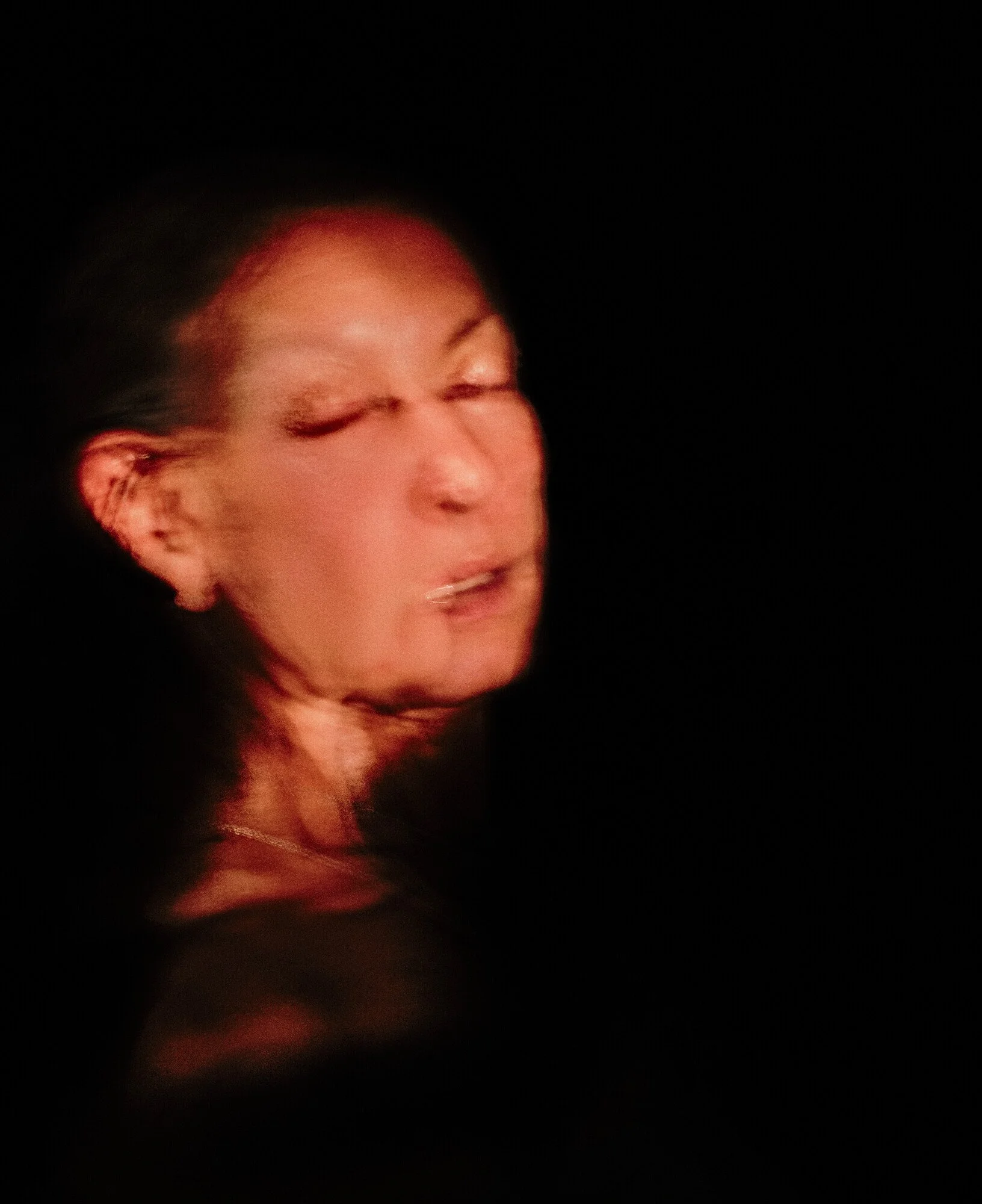 A woman with dark hair, with a blurred facial expression, against a black background.