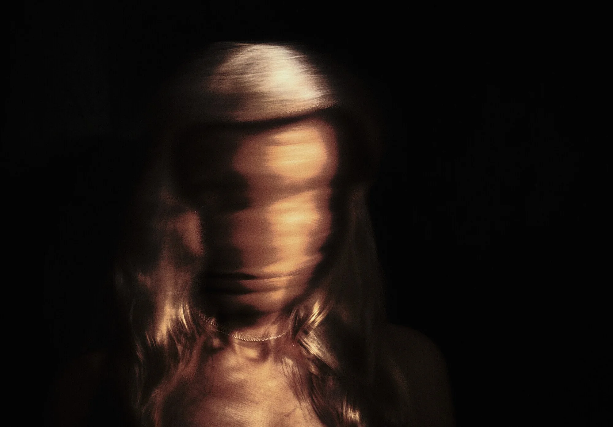 A blurred portrait of a woman with blonde hair, set against a black background.