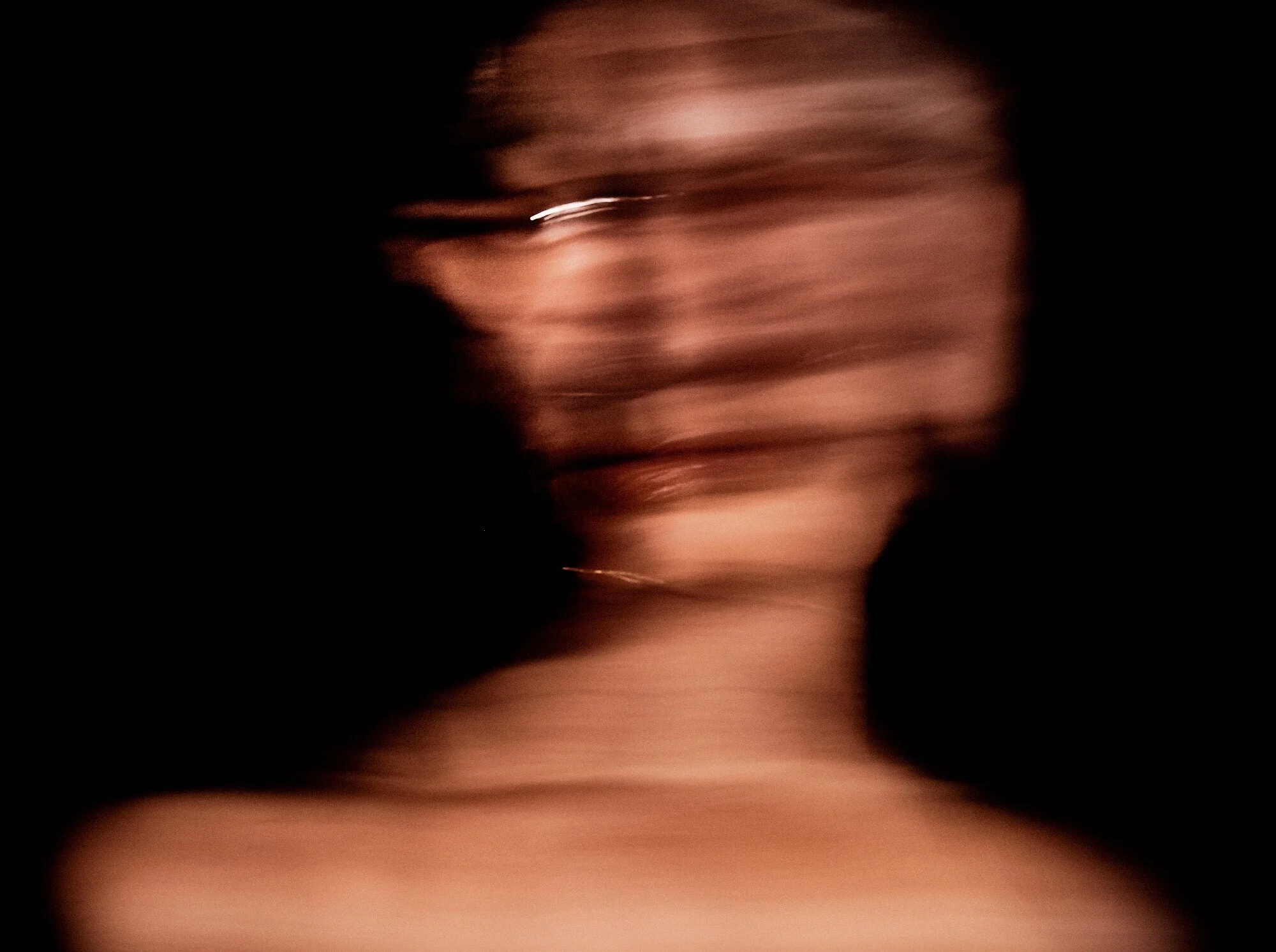 Blurred portrait of a woman with short hair, wearing gold hoop earrings, against a dark background.