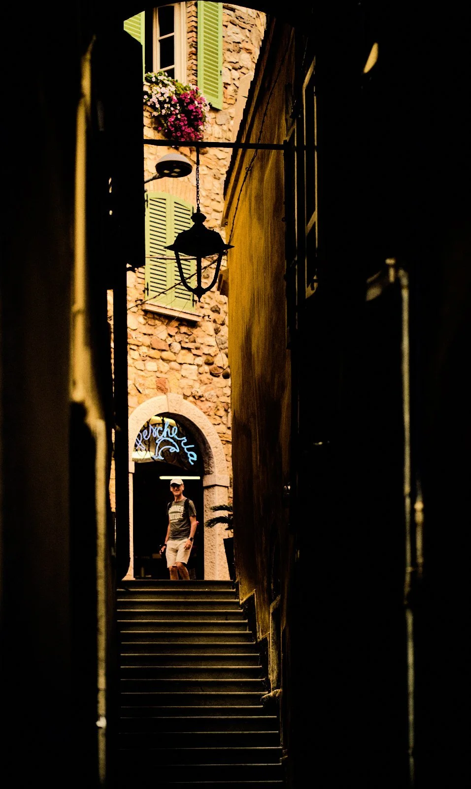 Neon Pescheria sign and stone facade with green shutters seen through a narrow dark passage with steps in Desenzano del Garda — Provincia Malinconica by Tom Imio
