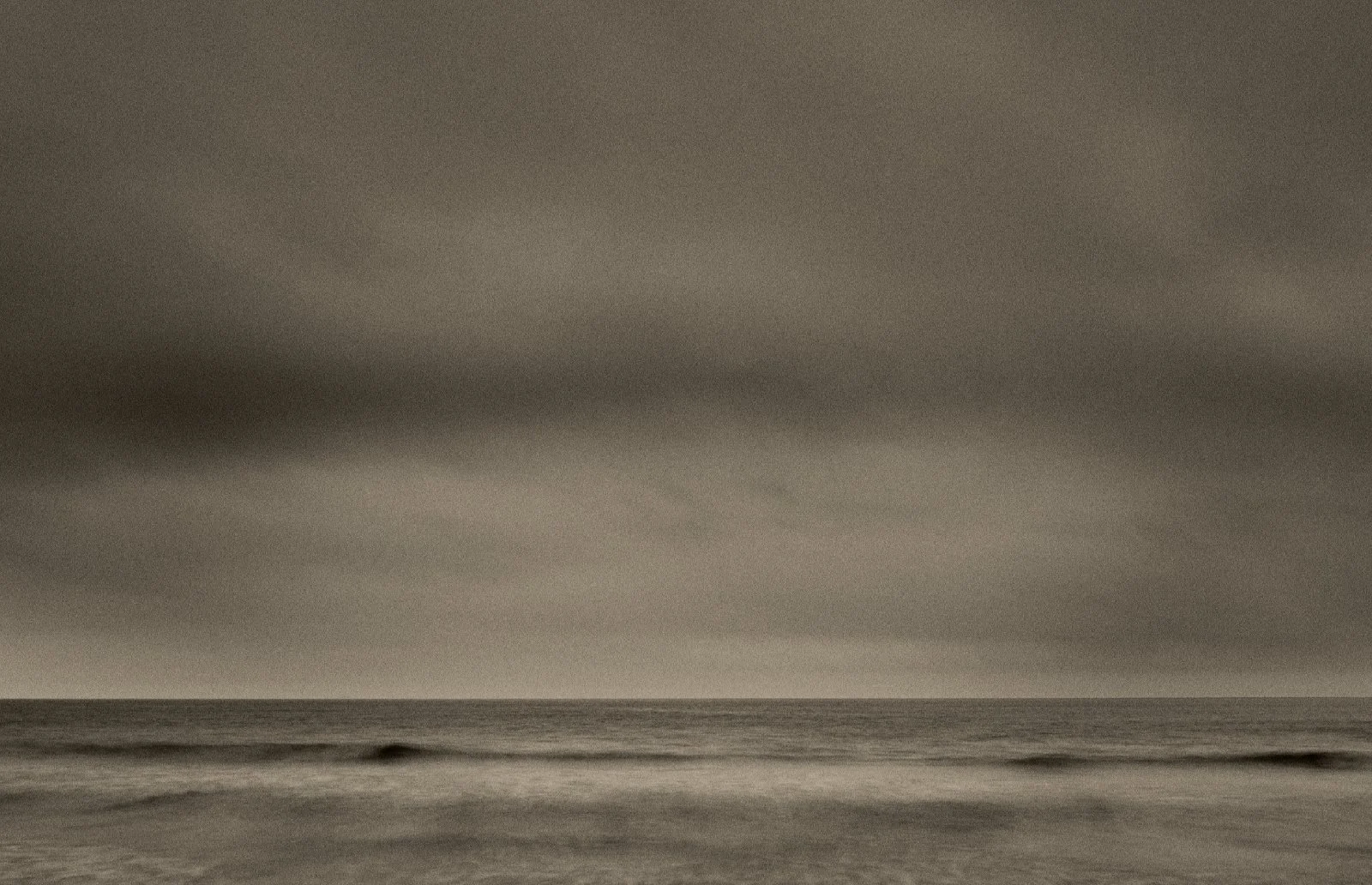 Long exposure seascape with soft waves under a heavy overcast sky in sepia tones — Mare Incognitum by Tom Imio