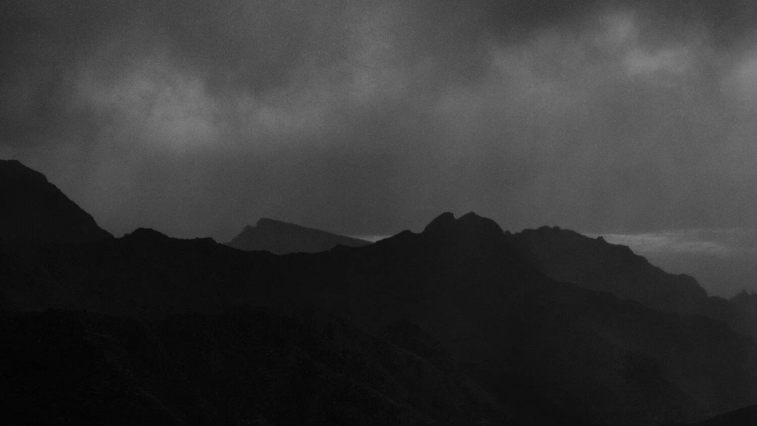 Black and white photo of a mountain range with a cloudy sky.