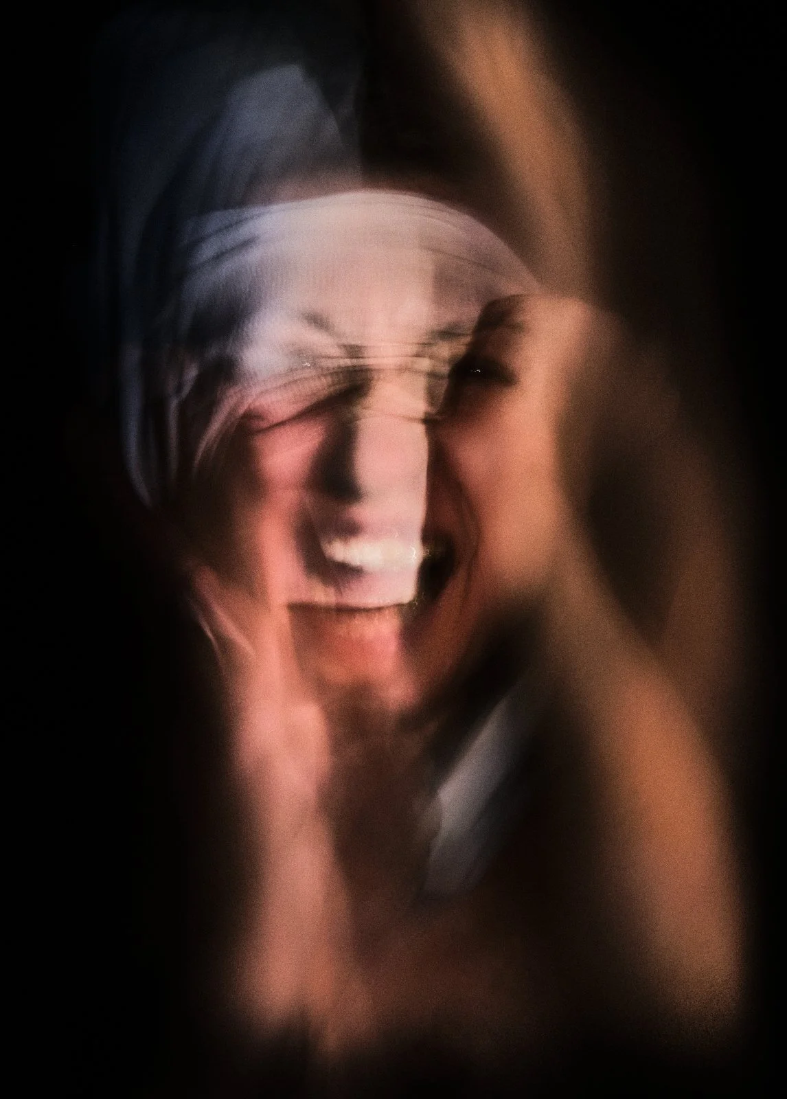 Blurred image of a person with short hair, smiling and laughing, with motion distortion and dark background.