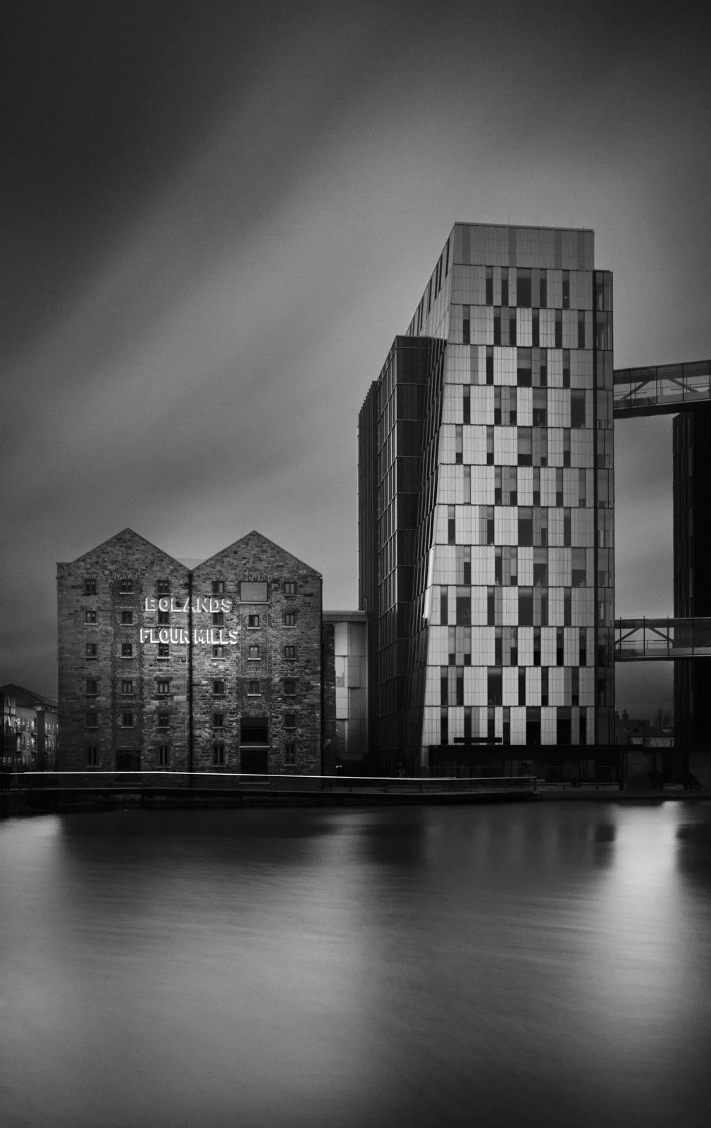 Black and white photo of modern buildings next to a water body, with one building labeled "EOLANGS FLOUR MILLS".
