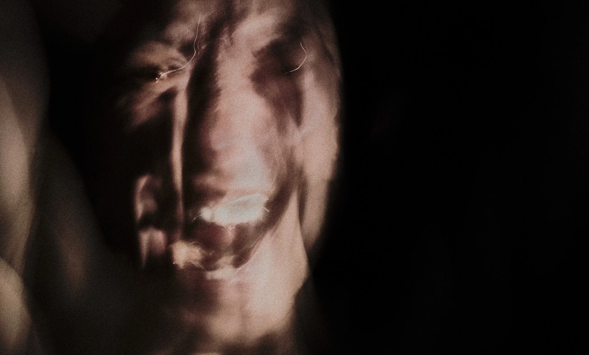 A person's face illuminated softly in a dark setting, with shadows creating a dramatic and mysterious atmosphere.