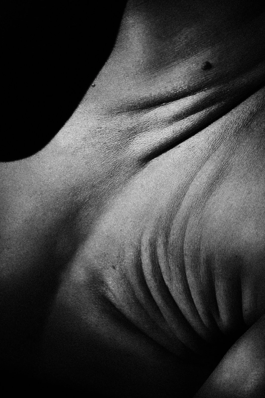 Black and white macro of soft skin folds and creases meeting in a shadowed valley, resembling a worn folded map