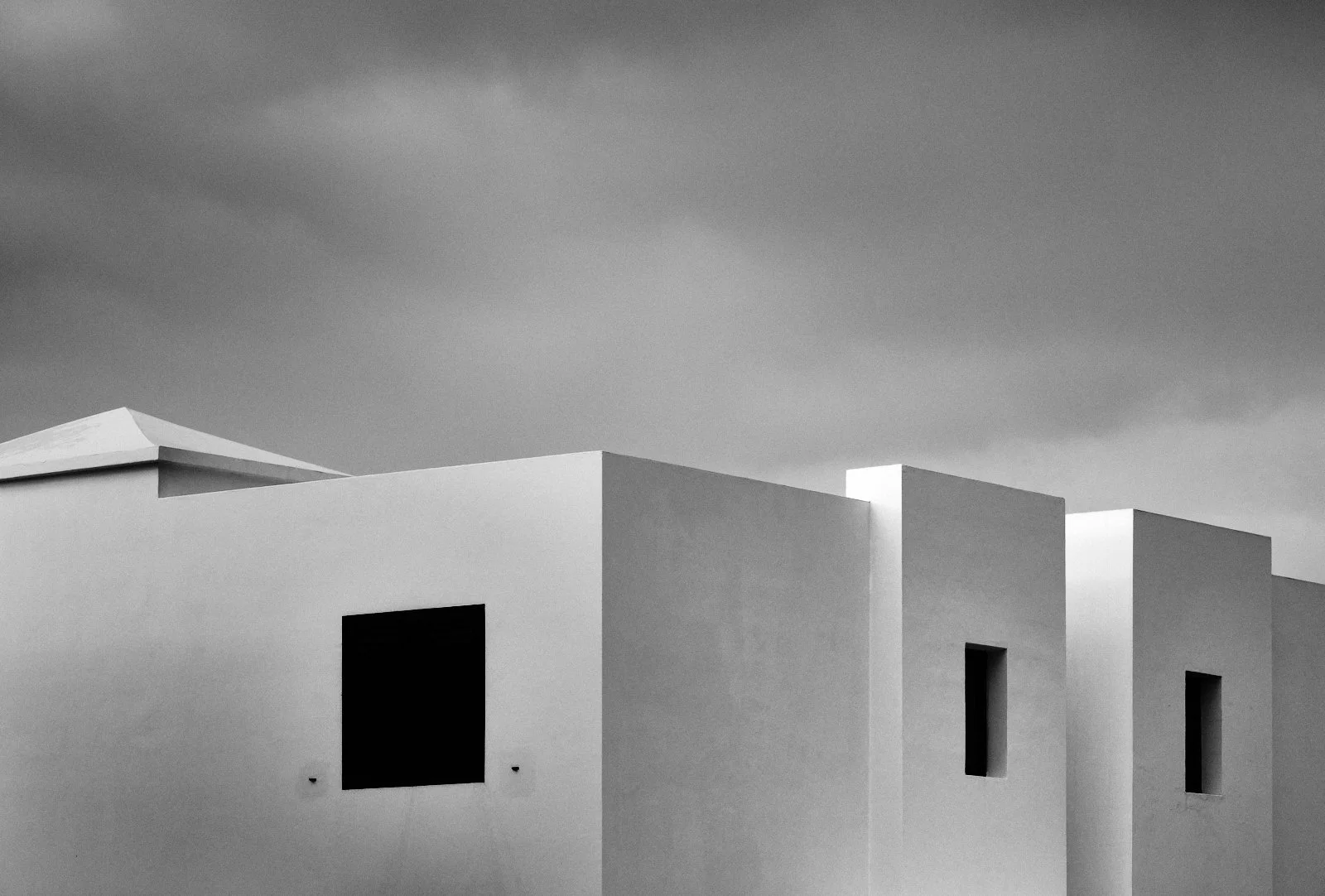 Black and white photo of modern white building with flat roof and rectangular windows under cloudy sky.