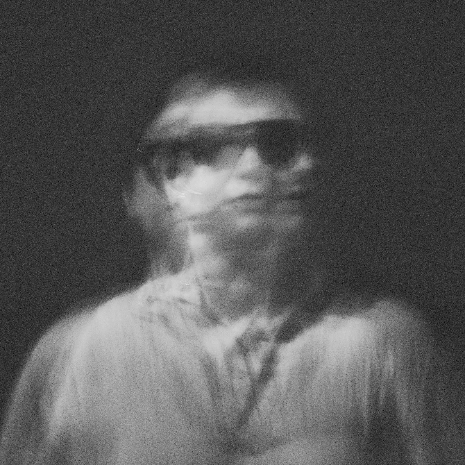 Double exposure black and white portrait of a person in a cap and sunglasses dissolving into darkness