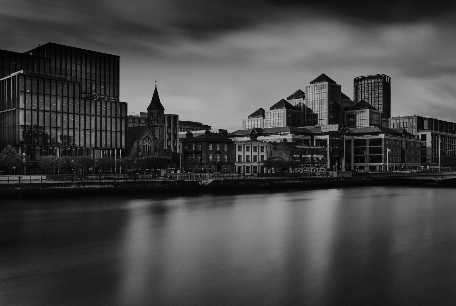 Black and white photo of city skyline with modern and historic buildings along a river.