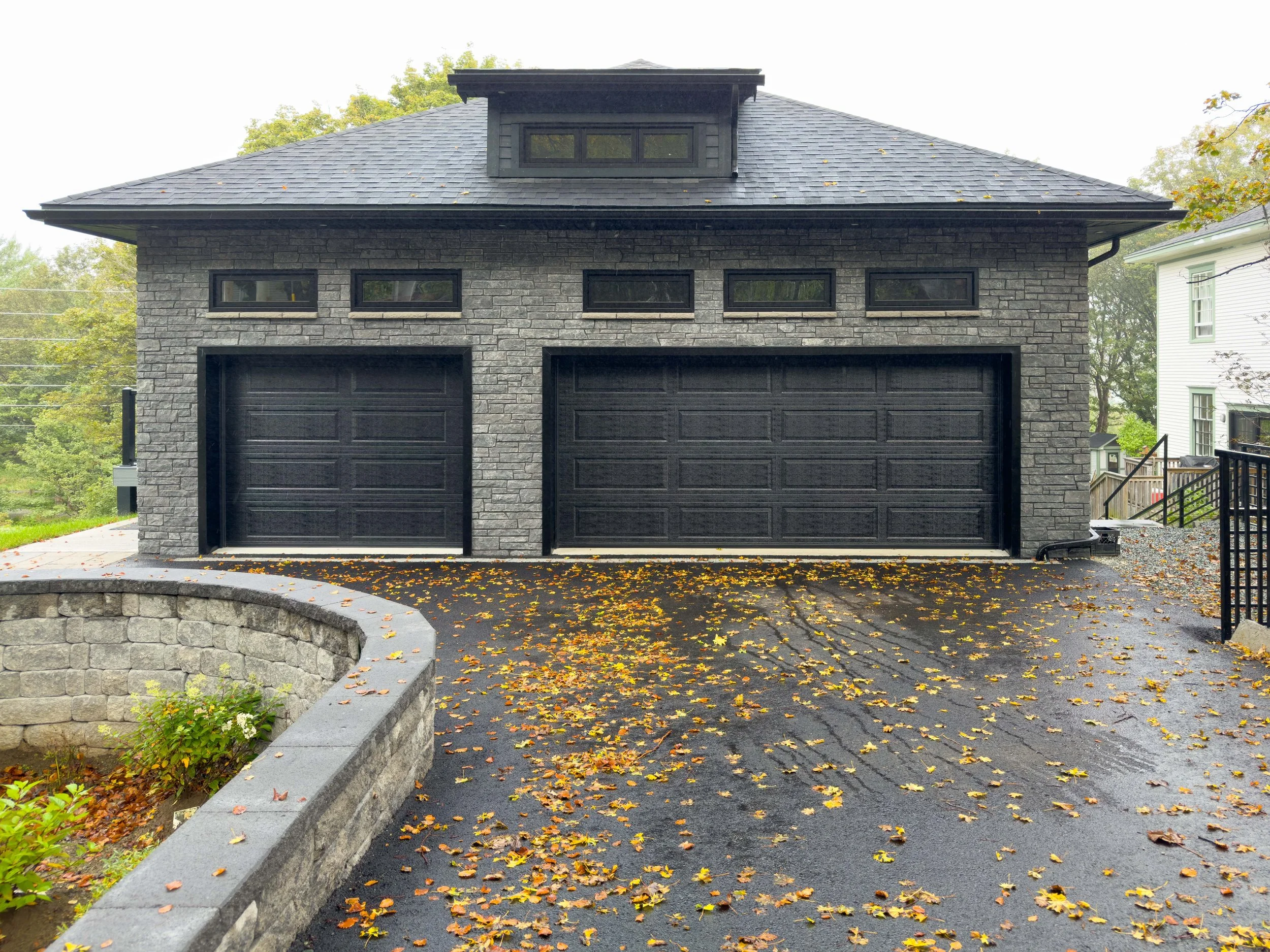 Modern black double garage doors installed on a gray stone home