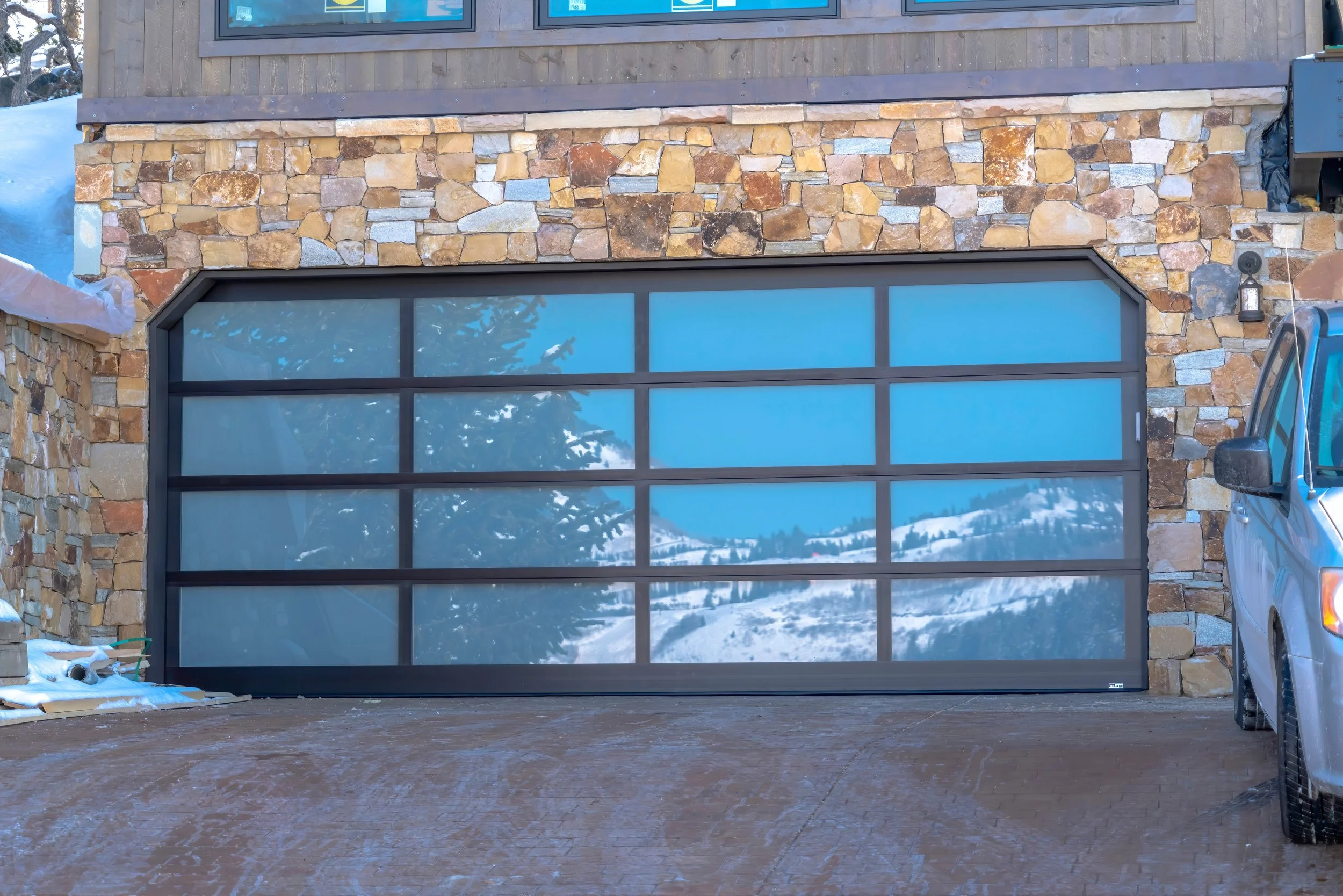 Modern black-framed glass panel garage door on a stone exterior home