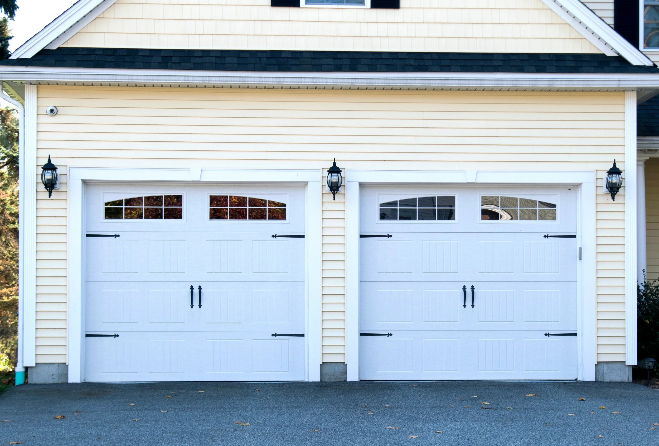 Classic white double garage doors with decorative hardware on a yellow siding home