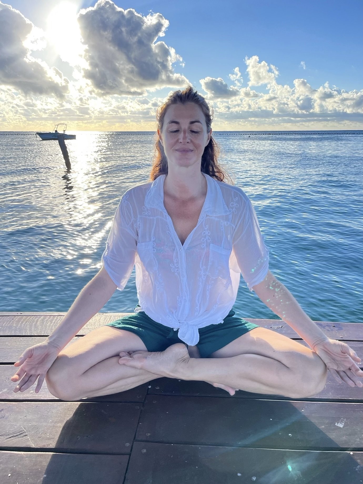 Lili Gavrilović sitting blissfully on a dock over water with the sun behind her.