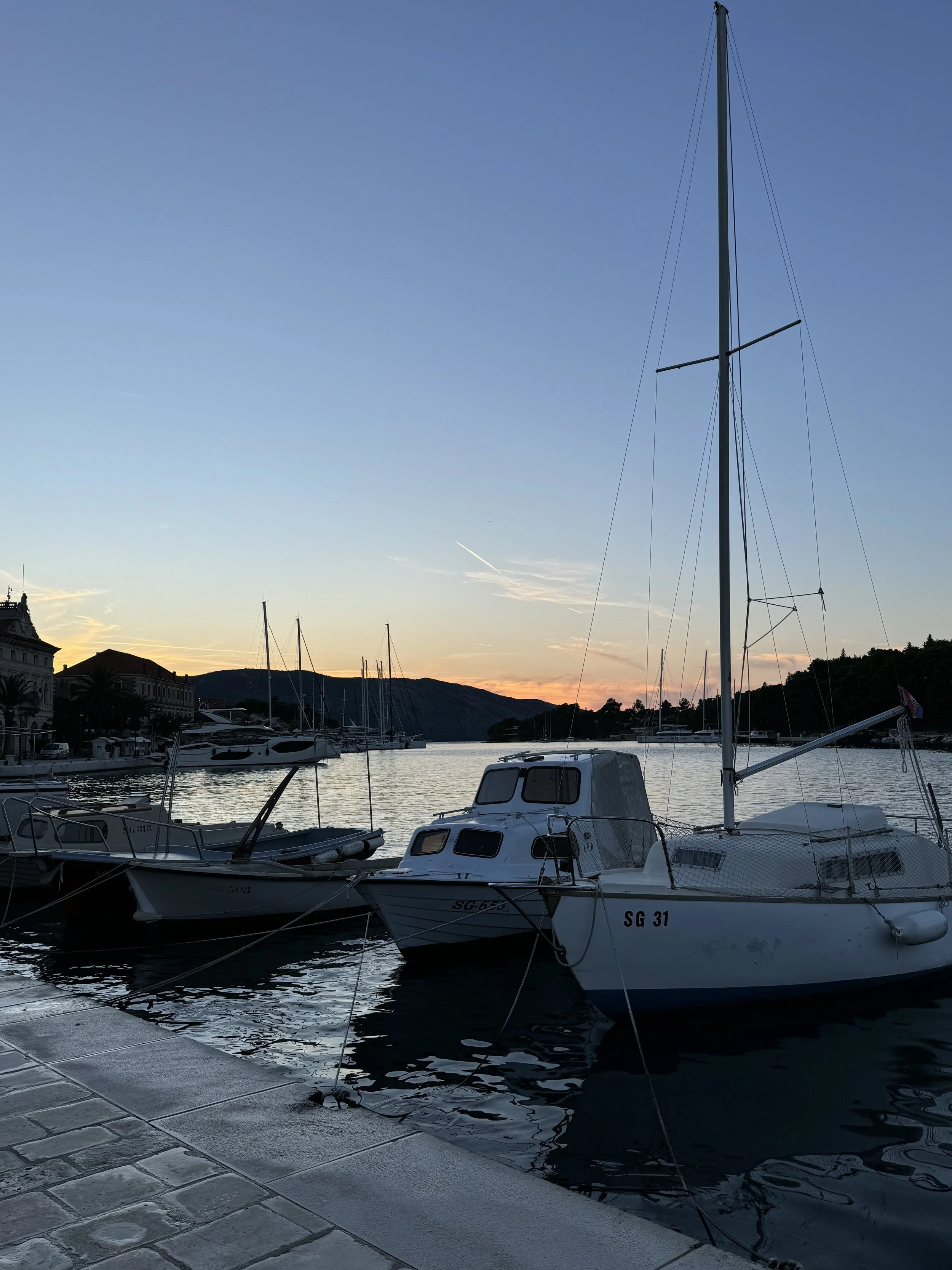 Boats docked at a marina during sunset with hills in the background.