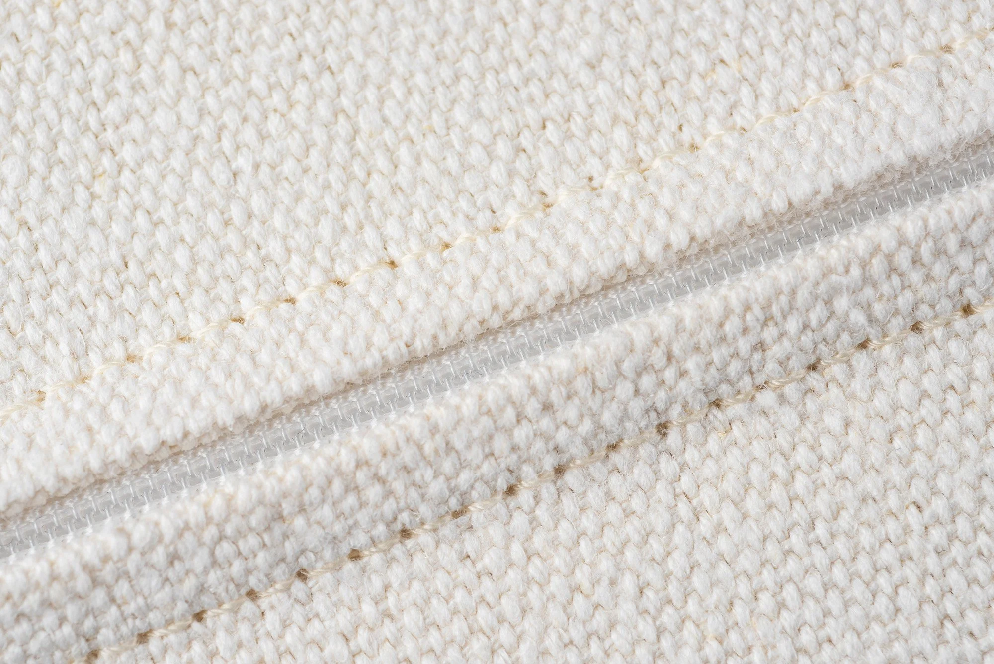 Nahaufnahme eines cremefarbenen Stoffes mit einer transparenten Reißverschluss. Die Textur des Stoffes ist baumwollartig mit einer dicken, groben Webart.