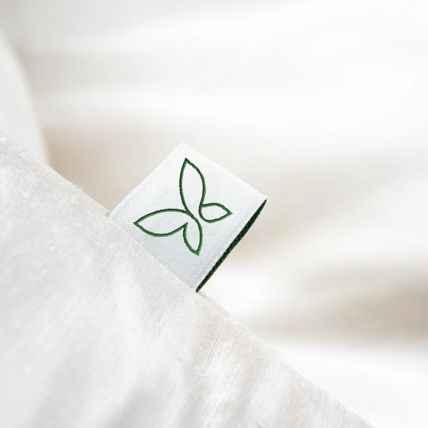 Nahaufnahme eines weißen Stoffetiketts mit grüner Baum- oder Blattform, das aus einem weißen Stoffbezug hervorlugt.
