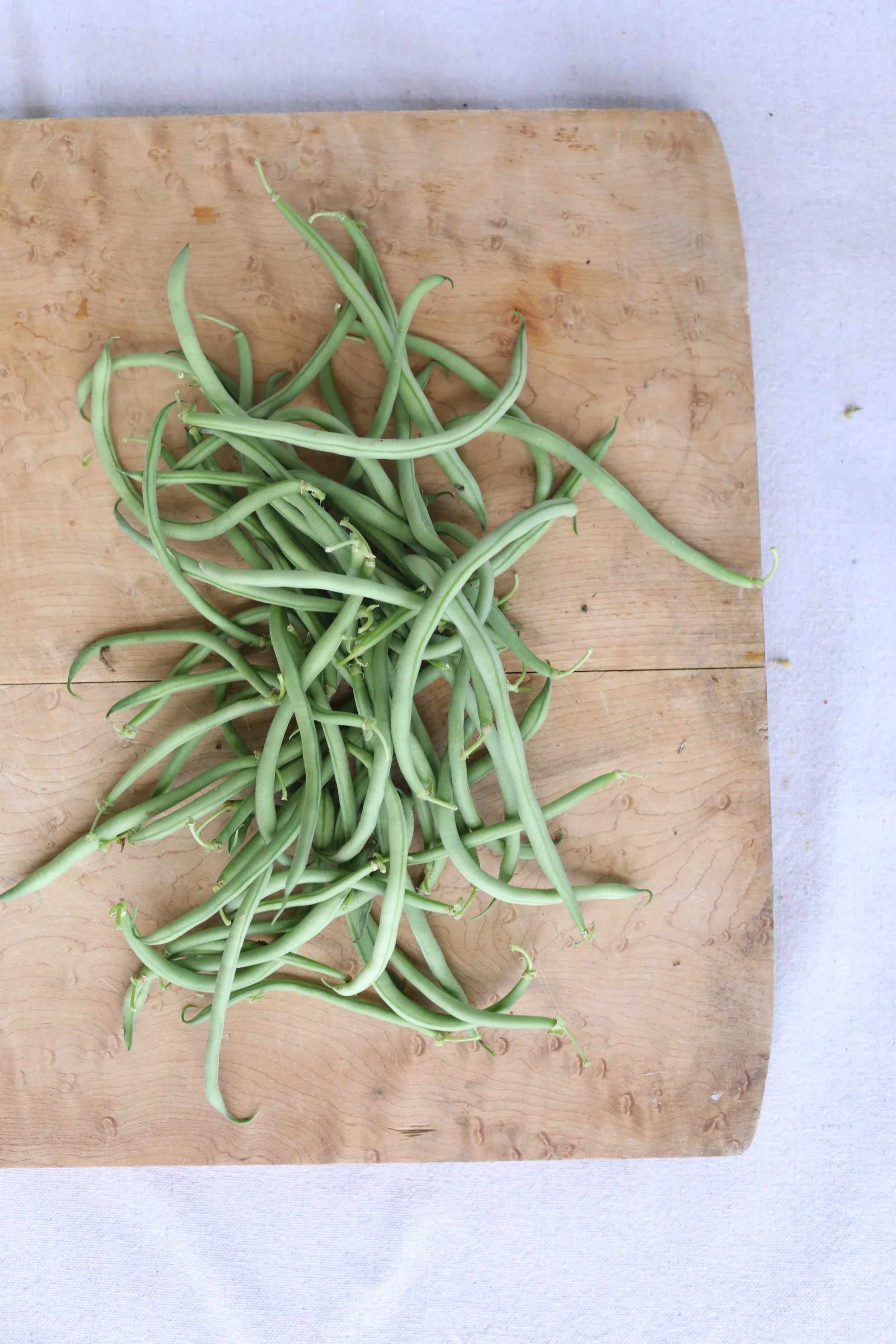 Fresh green beans on a wooden cutting board.