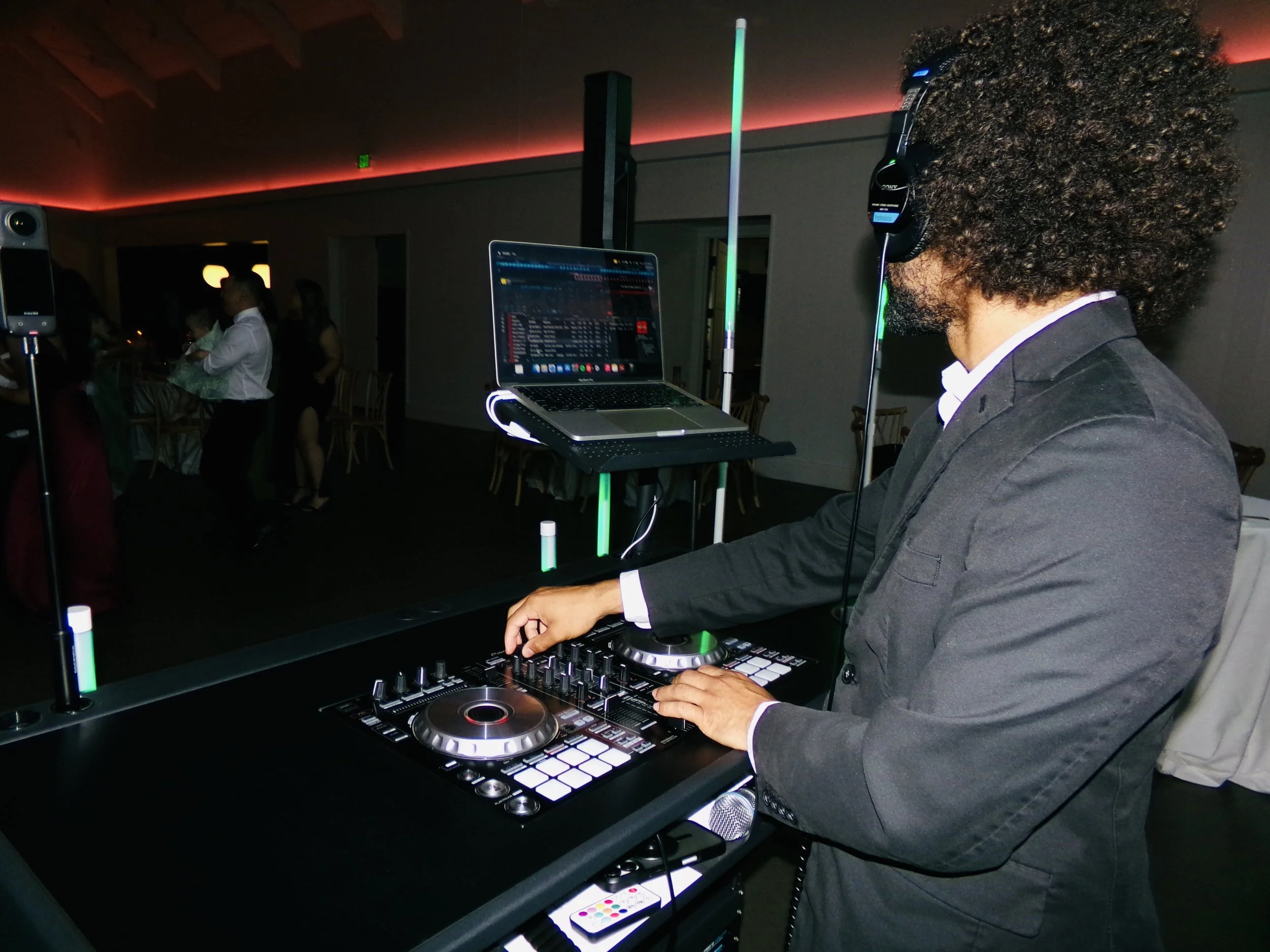 Premium DJ Noah, DJ Northh professionally mixing, standing outdoors at night surrounded by trees, working at a DJ booth with DJ equipment, with blue lights and a DJ set up behind him.