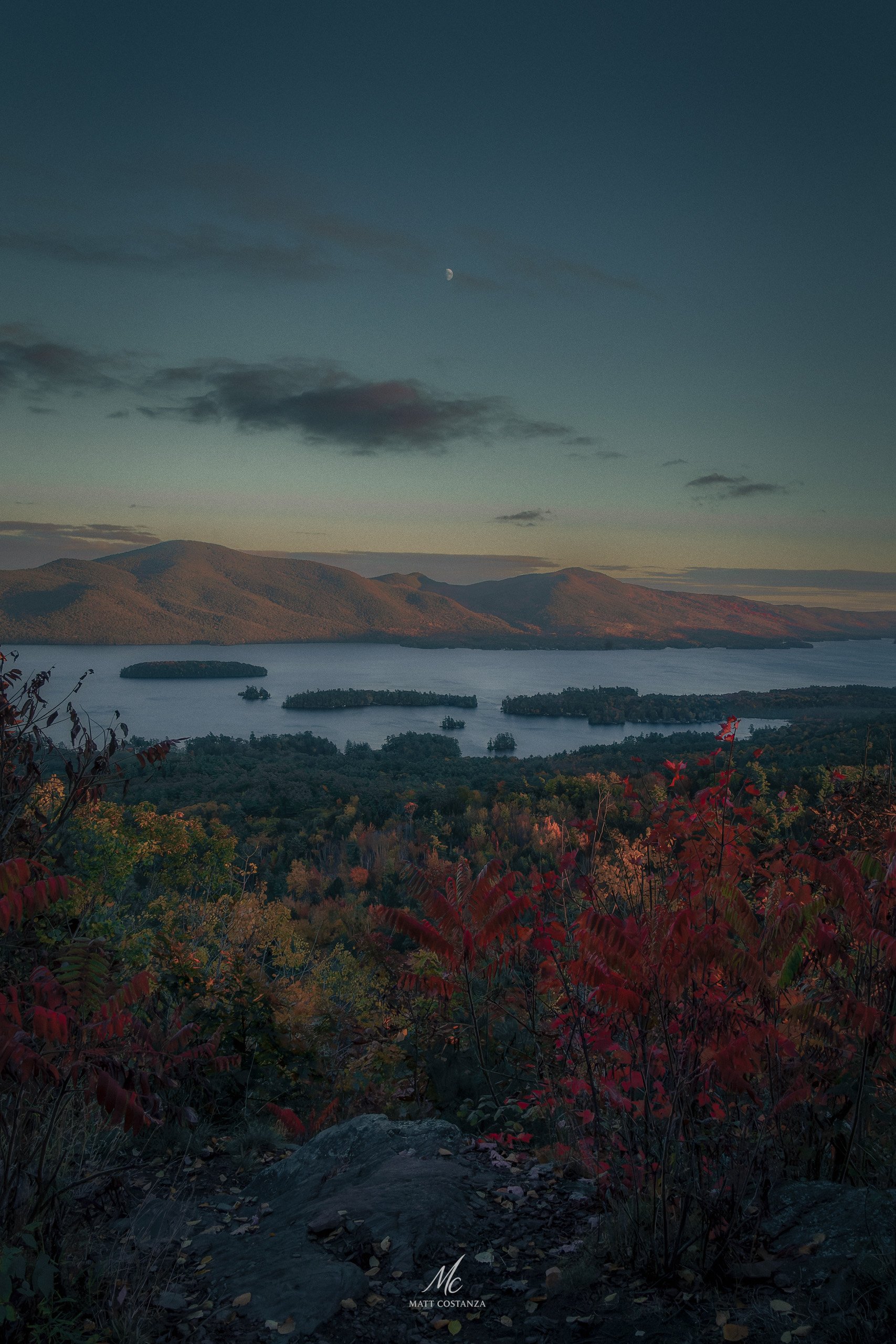 View from The Pinnacle in the Adirondacks overlooking lakes and islands framed by autumn foliage and distant mountain ranges