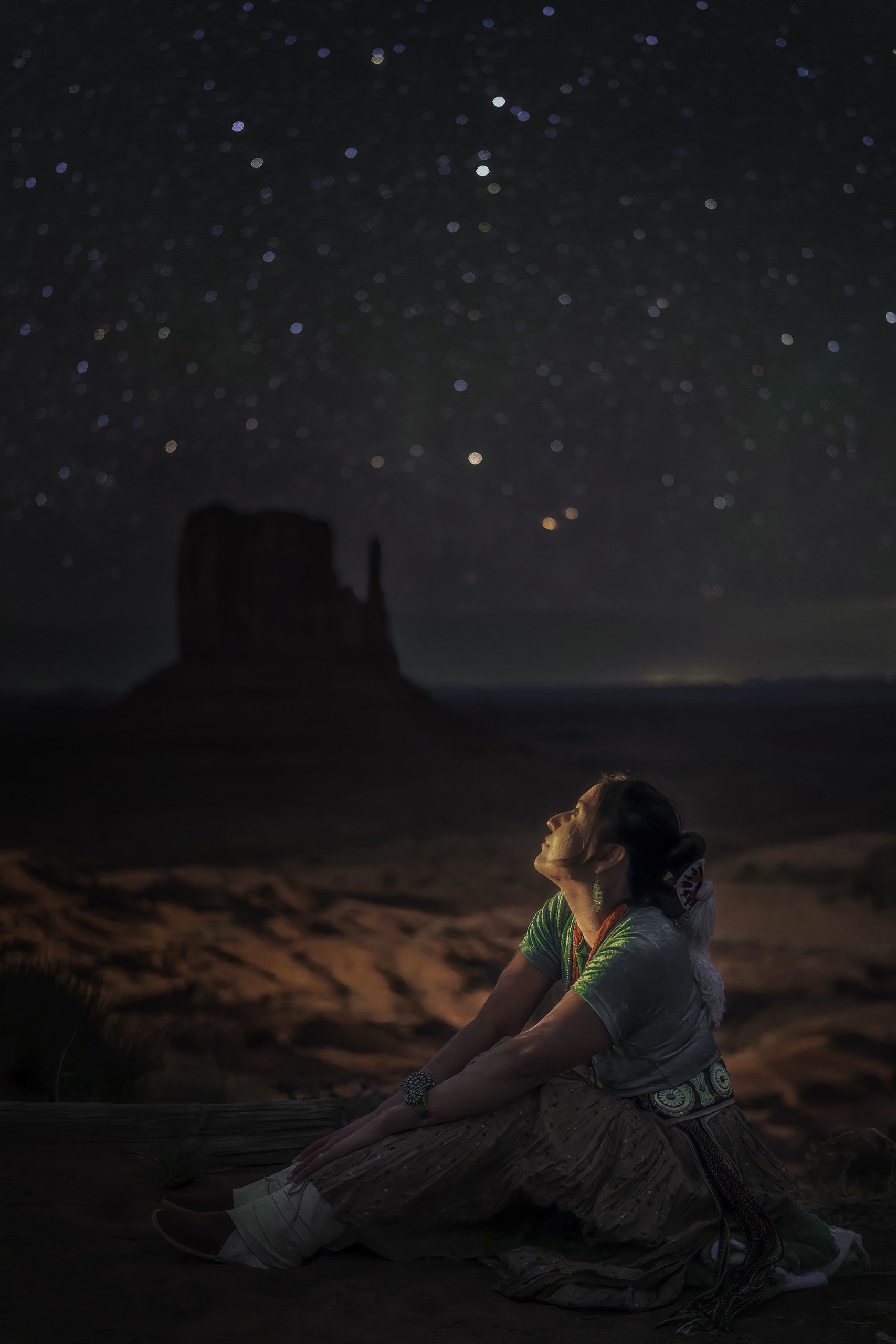 Portrait of a Navajo woman in traditional dress under a starry night sky in Monument Valley, Utah, with sandstone buttes silhouetted in the background, photographed by Matt Costanza.