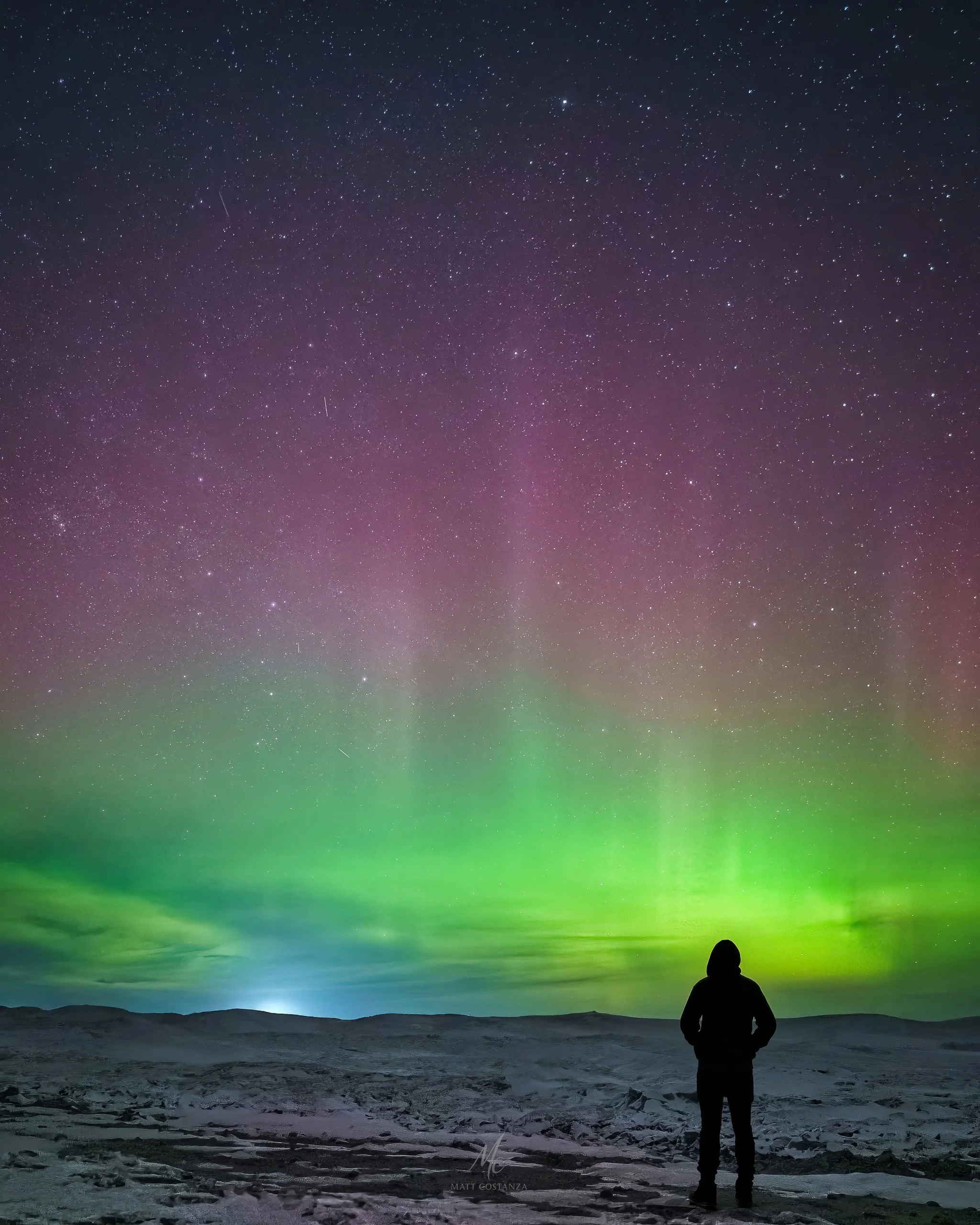 Silhouetted figure under green and magenta aurora at Whitefish Point, Michigan.