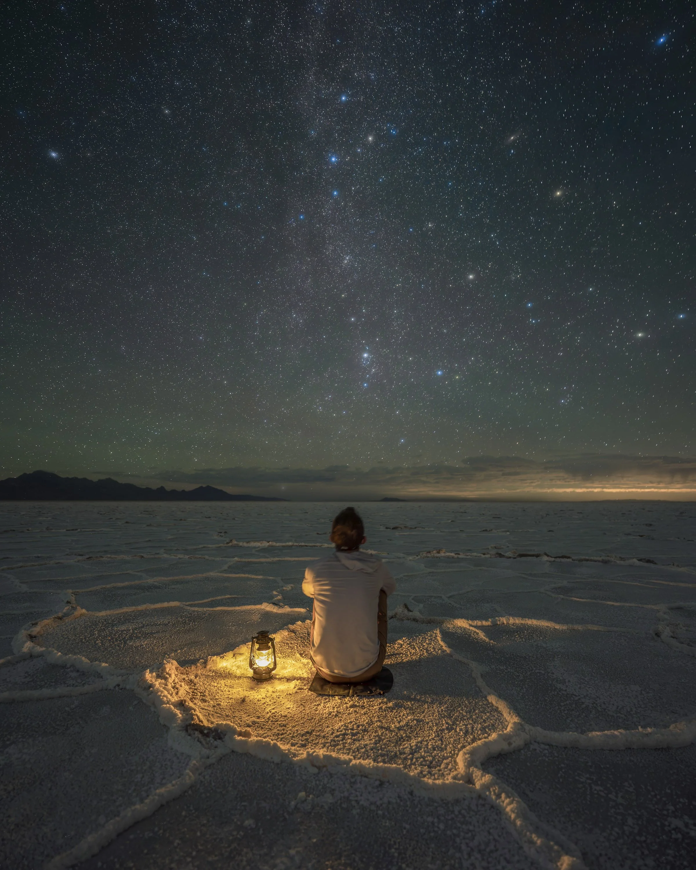Landscape astrophotography self-portrait sitting beside a lantern under the star-filled night sky at the Bonneville Salt Flats in Utah