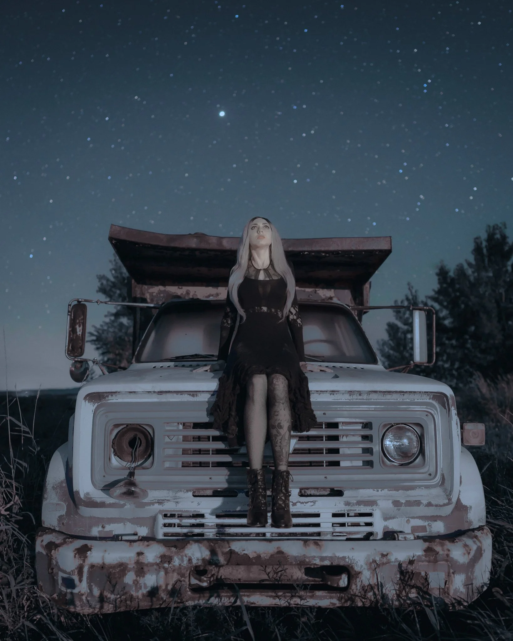 Woman on a vintage truck under a star-filled night sky.