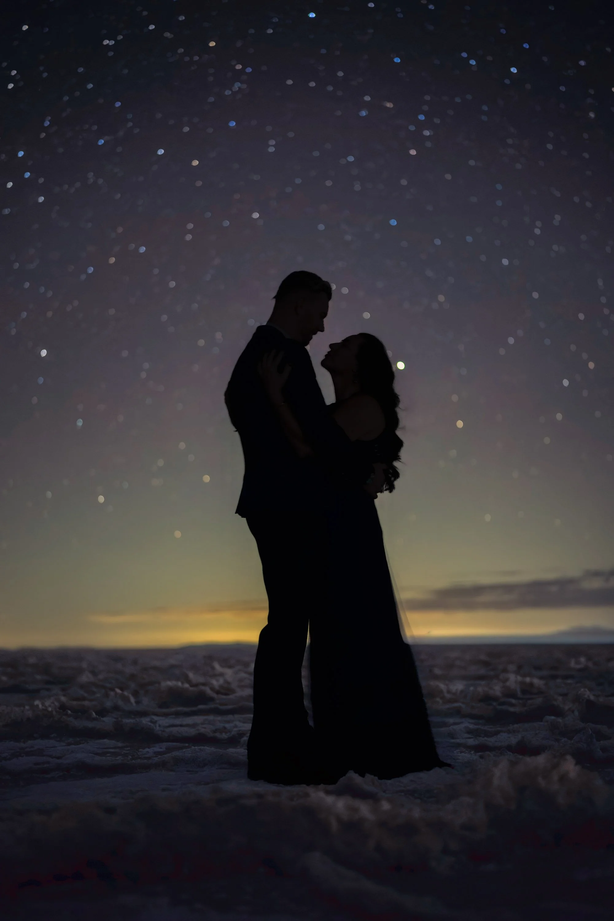 Silhouette of a couple embracing beneath a star-filled night sky at the Bonneville Salt Flats in Utah.