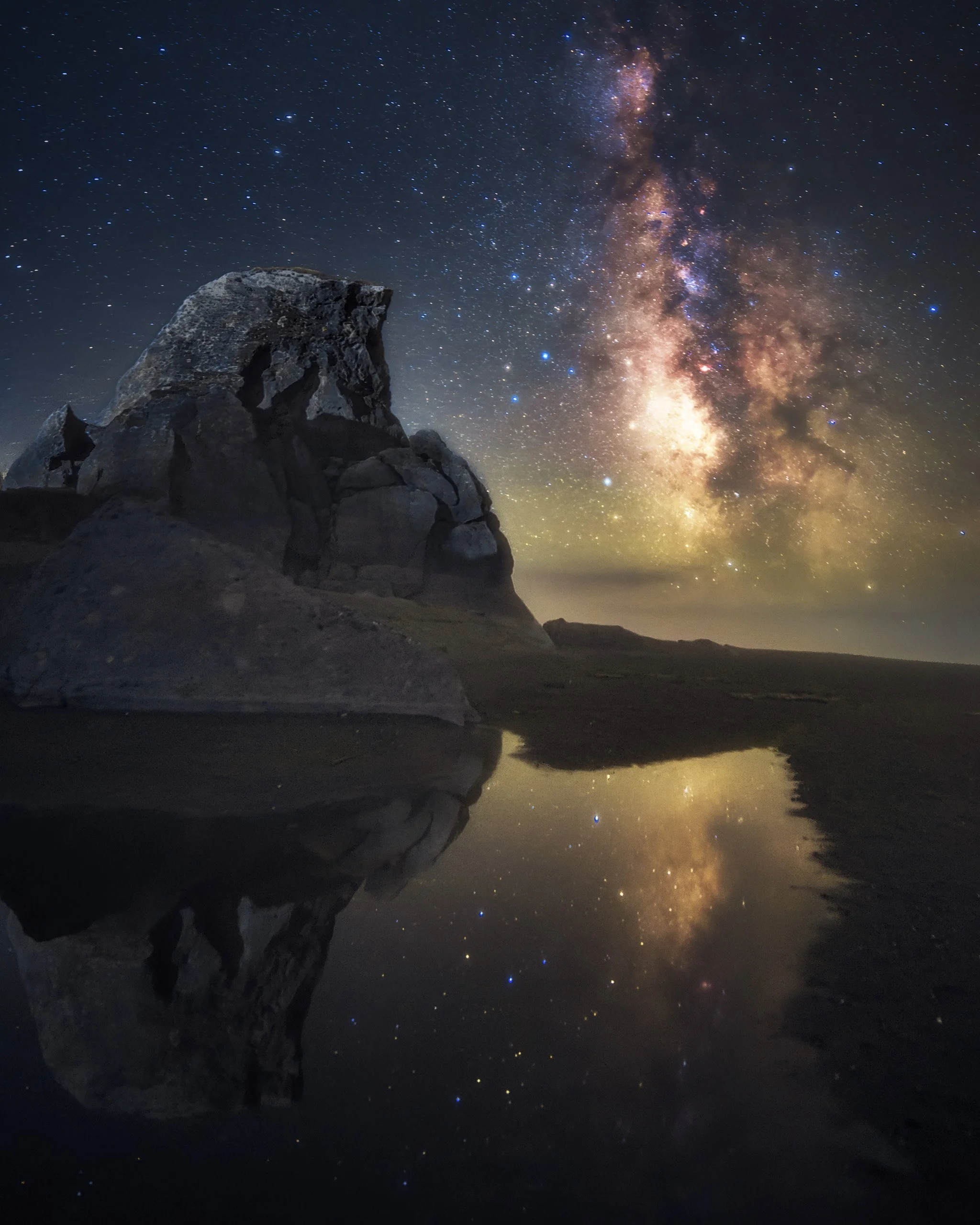 Milky Way galaxy reflected in a tidal pool beneath Kissing Rock on the Oregon coast at night, with stars mirrored in the water and the rock formation silhouetted, photographed by Matt Costanza.