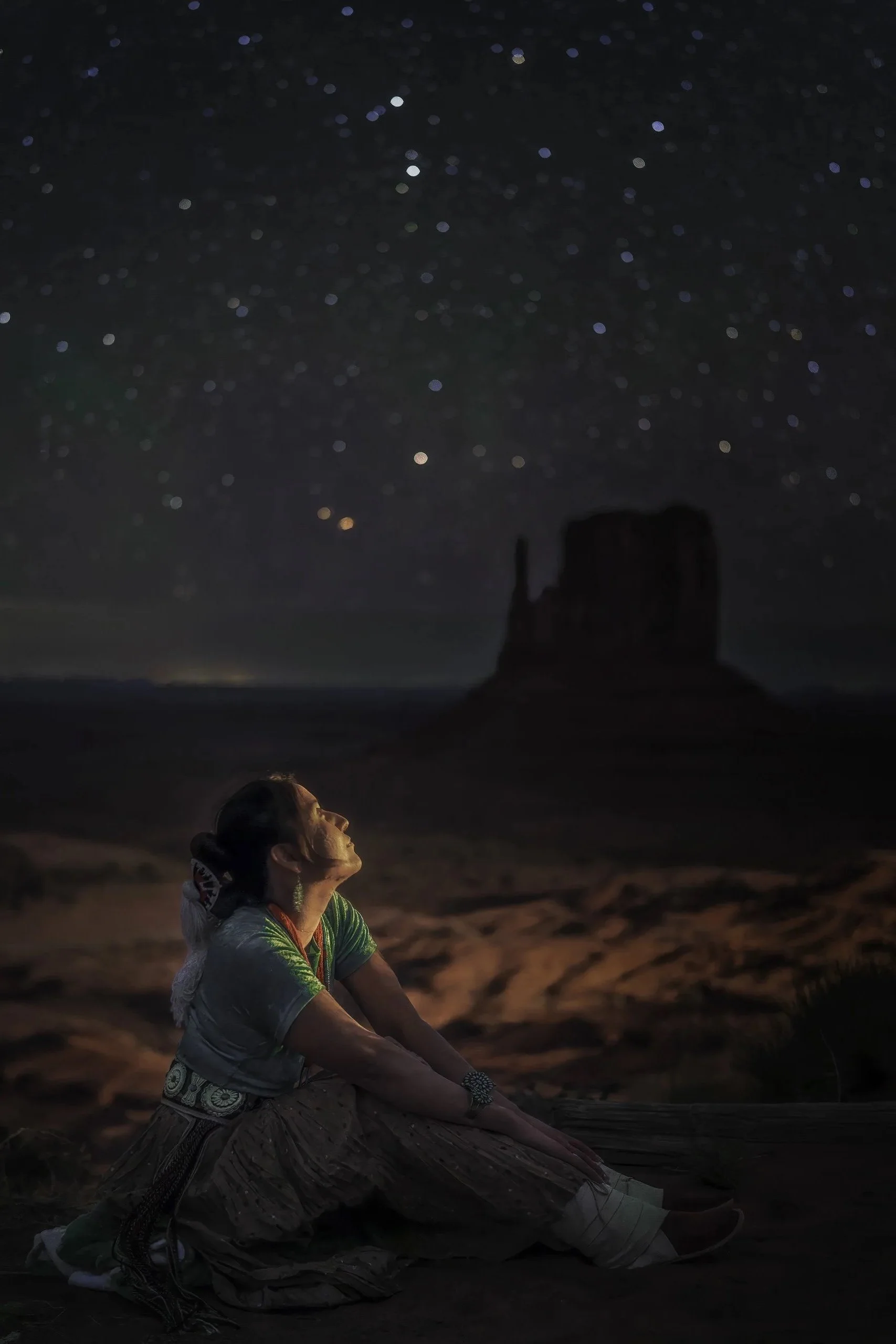 Portrait of a Navajo woman in traditional dress under a starry night sky in Monument Valley, Utah, with sandstone buttes silhouetted in the background, photographed by Matt Costanza.