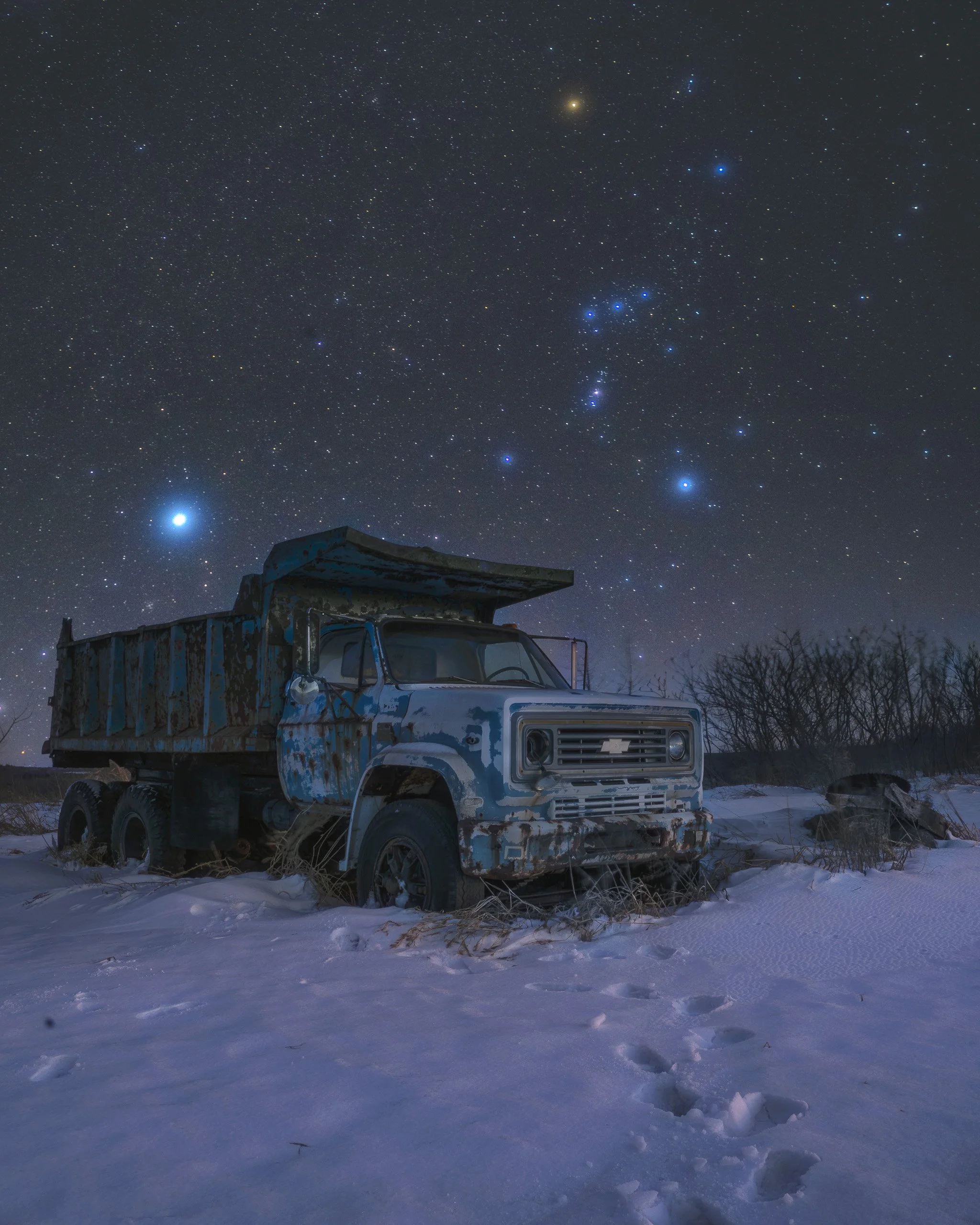 Rusty abandoned truck in a snowy field under a clear night sky with the Orion constellation visible above in rural New York, photographed by Matt Costanza.
