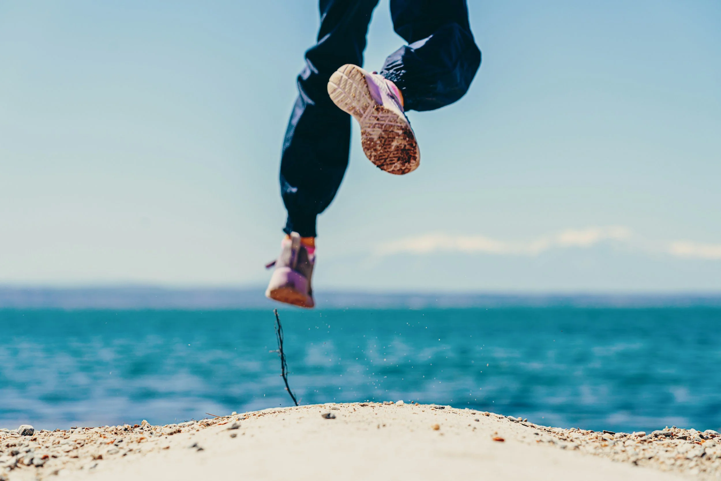 A happy person jumping on the sand on their way to sea.