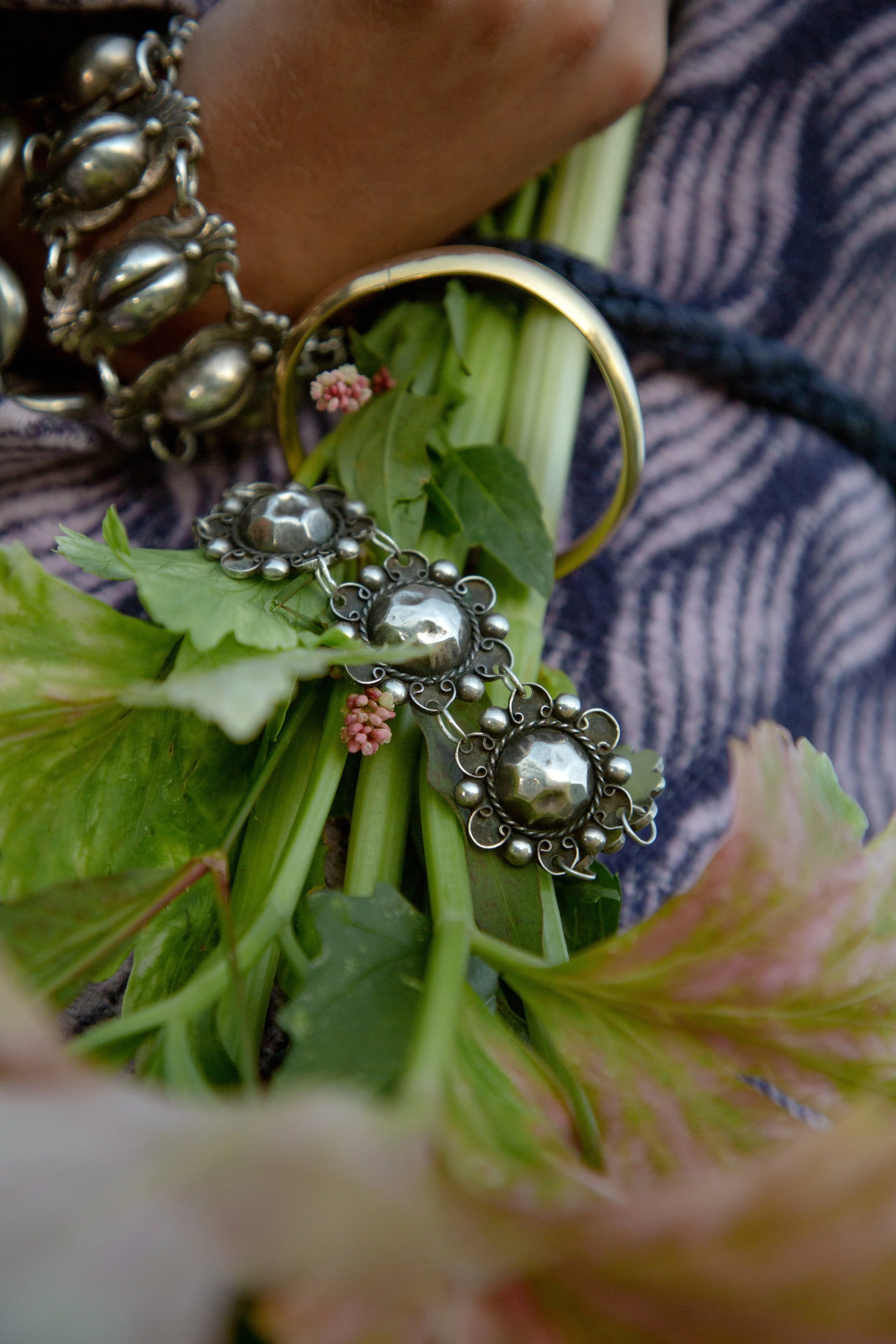 Close-up of silver jewelry, including a bracelet and a ring, laid on green leaves and flowers.
