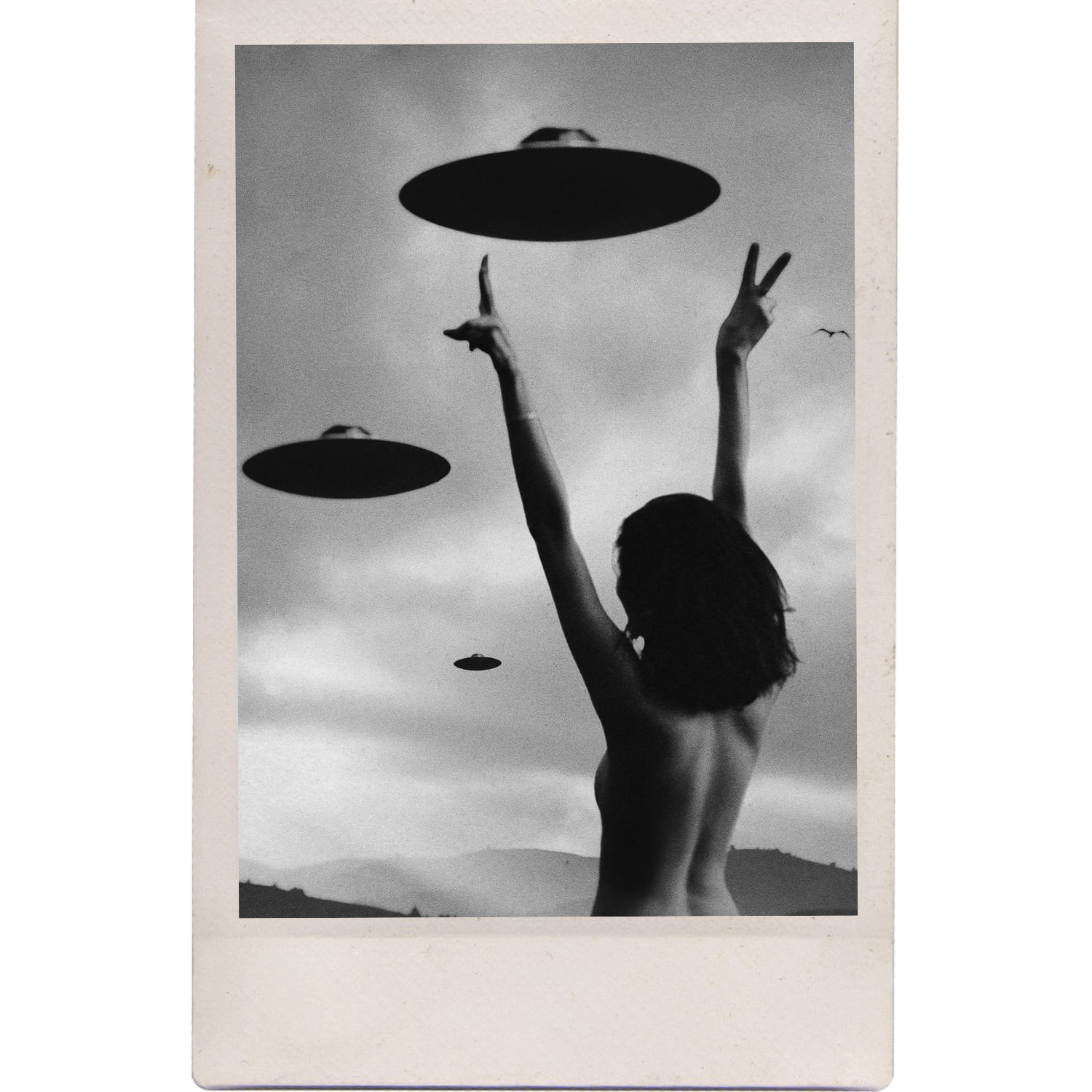 A black-and-white photo of a woman with short hair, standing outdoors against a backdrop of mountains and cloudy sky, with her arms raised above her head, making peace signs with her fingers. Multiple UFO-shaped objects are floating in the sky around her.