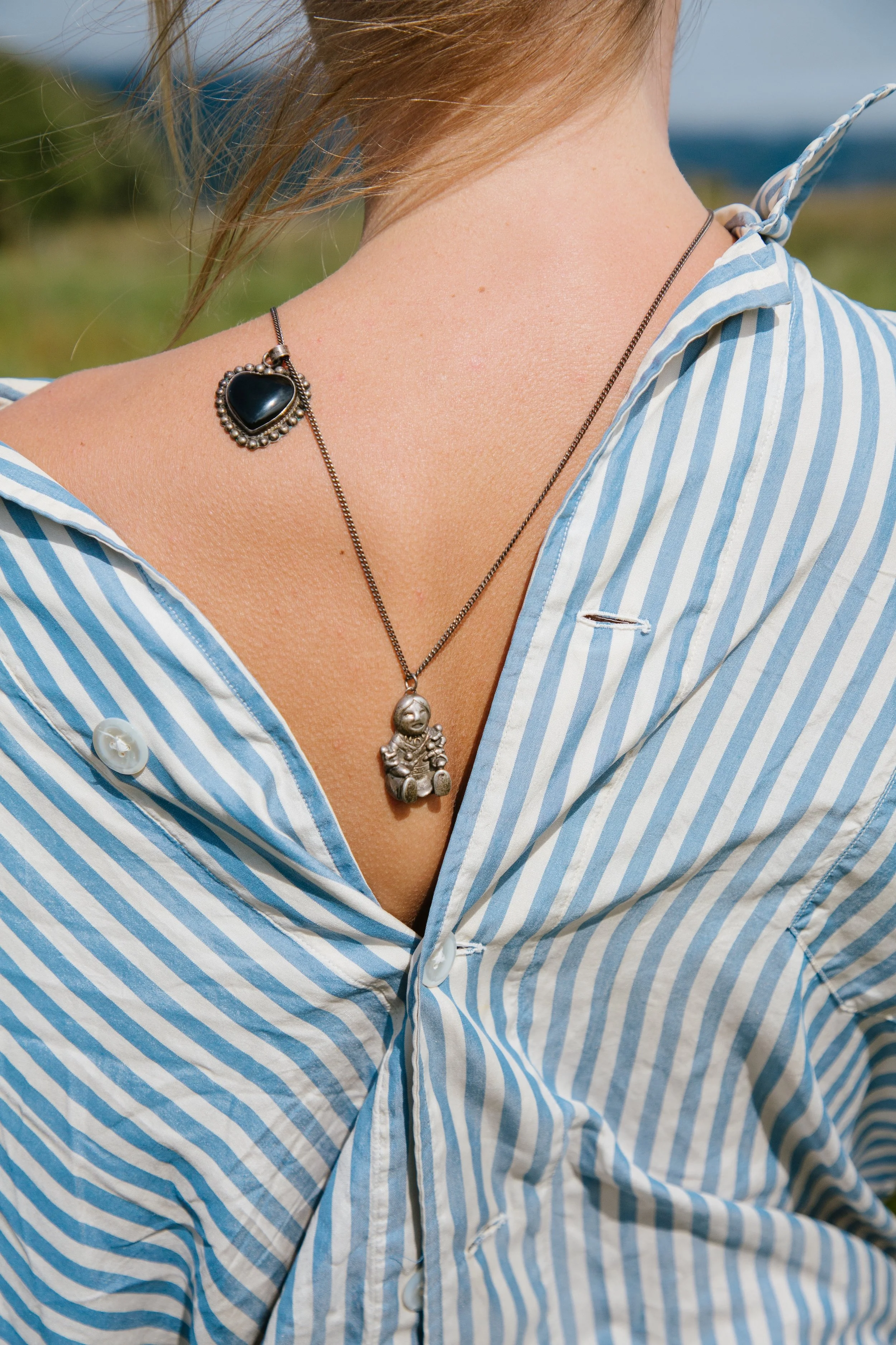 Close-up of a woman wearing a blue and white striped shirt with a heart-shaped pendant necklace.