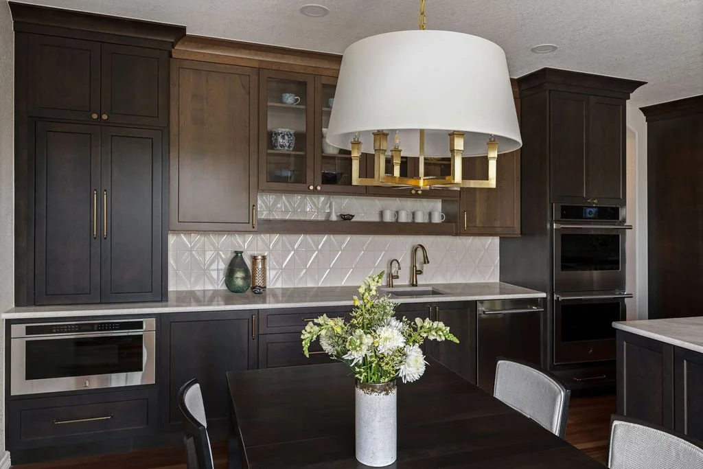 Elegant kitchen with dark wood cabinetry, white tile backsplash, statement lighting, and a cozy dining area.