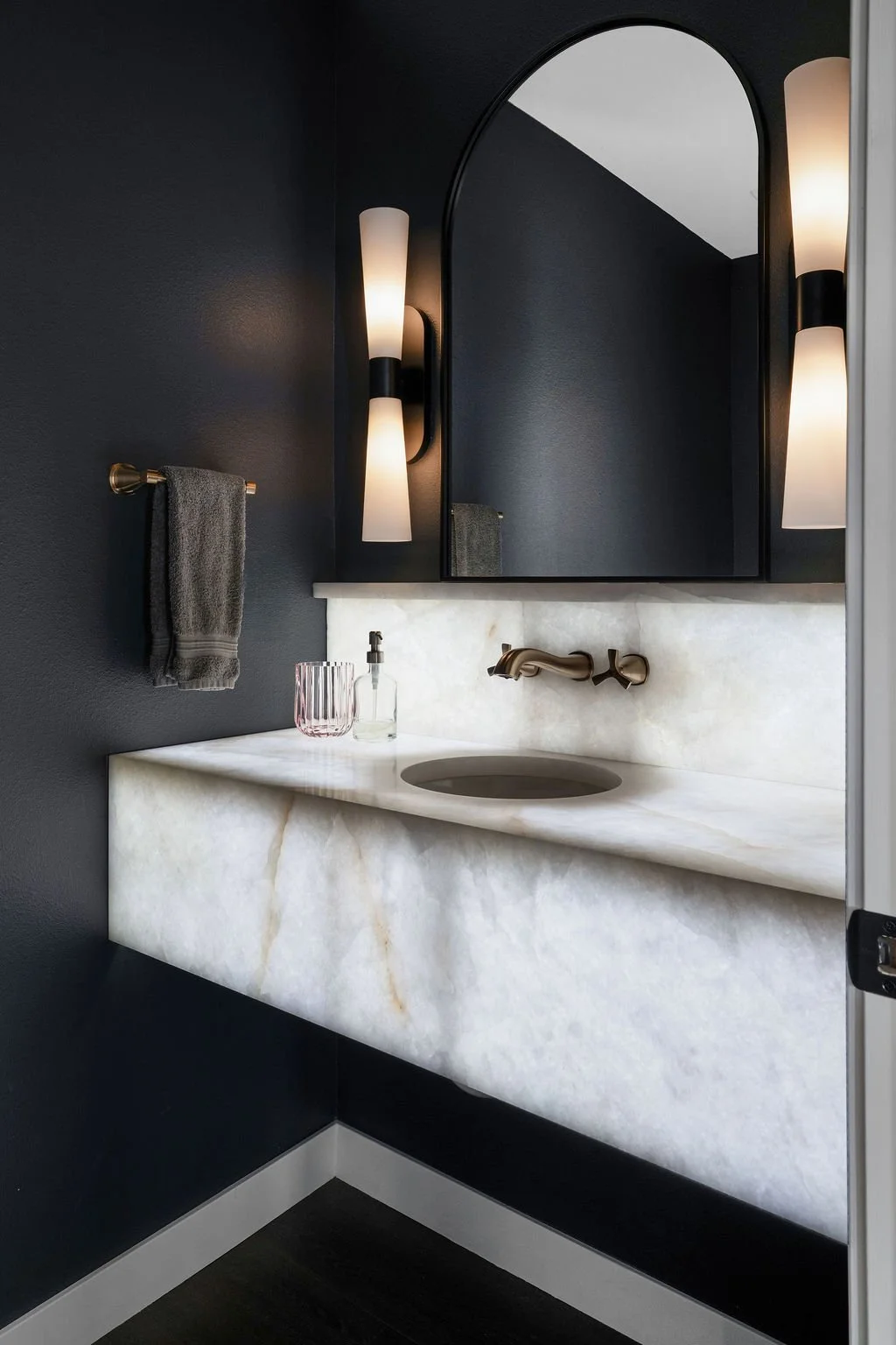 Sophisticated powder bathroom featuring dramatic dark walls, floating marble vanity, warm modern lighting, and refined contemporary finishes.