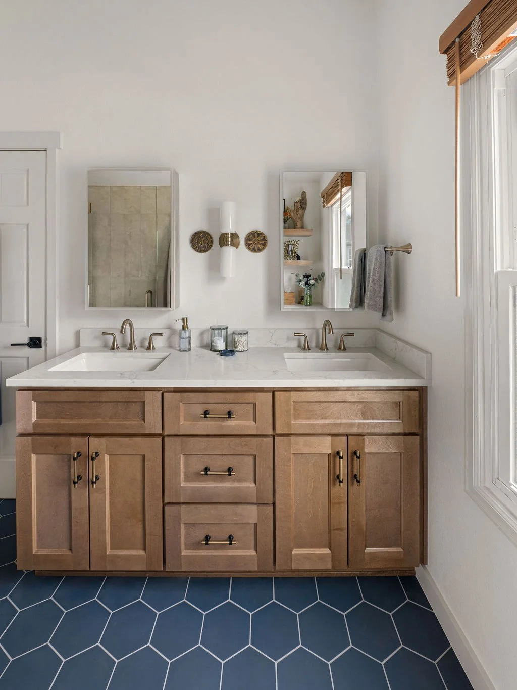 Remodeled bathroom with natural wood cabinetry, floating wood shelves, blue hexagon floor tile, and warm wood window blinds