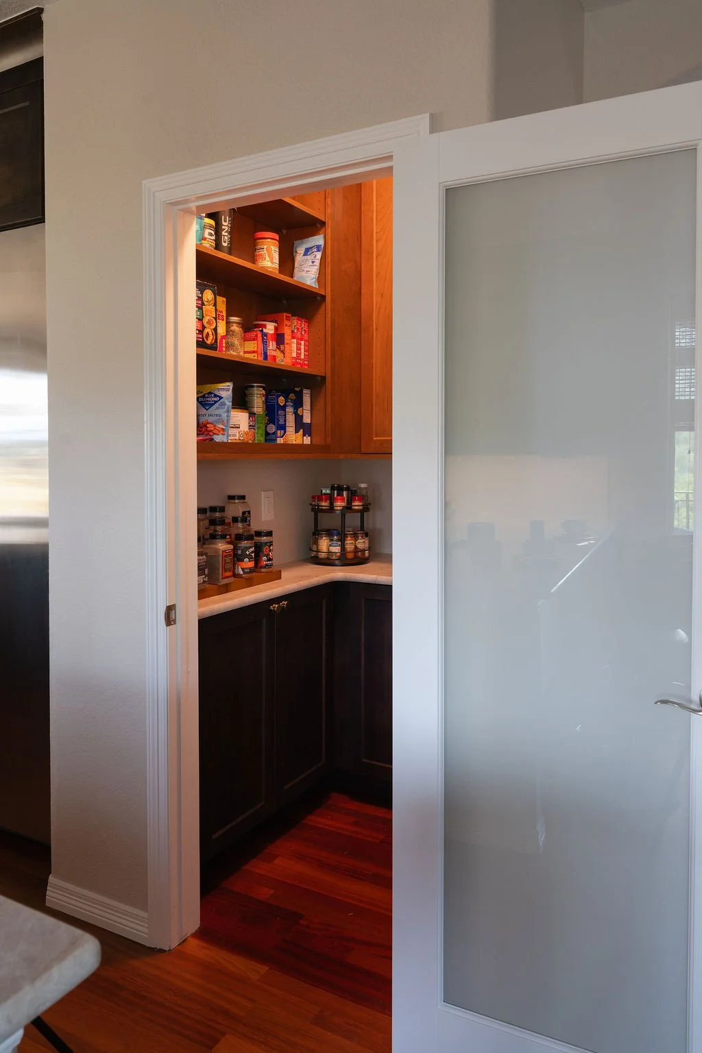 Walk-in pantry with built-in cabinetry, open shelving, countertop storage, and a frosted glass door.