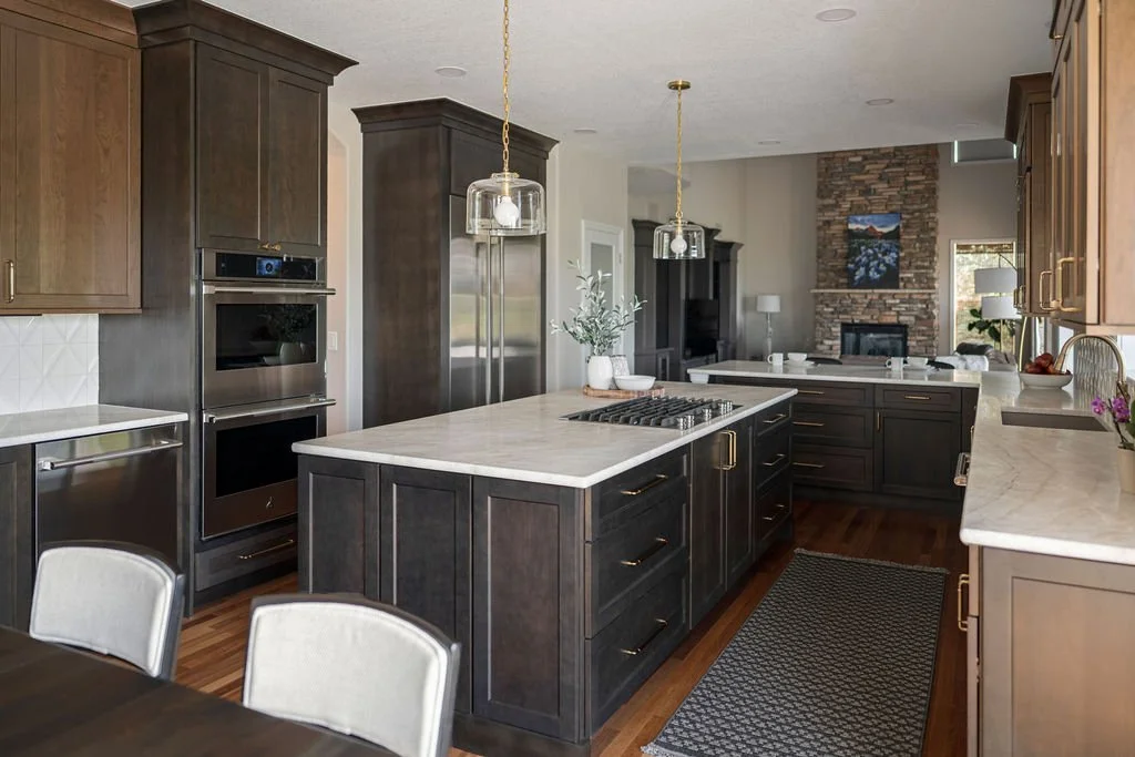 Modern kitchen with dark woodland cabinetry, large stone island, stainless steel appliances, and pendant lighting.