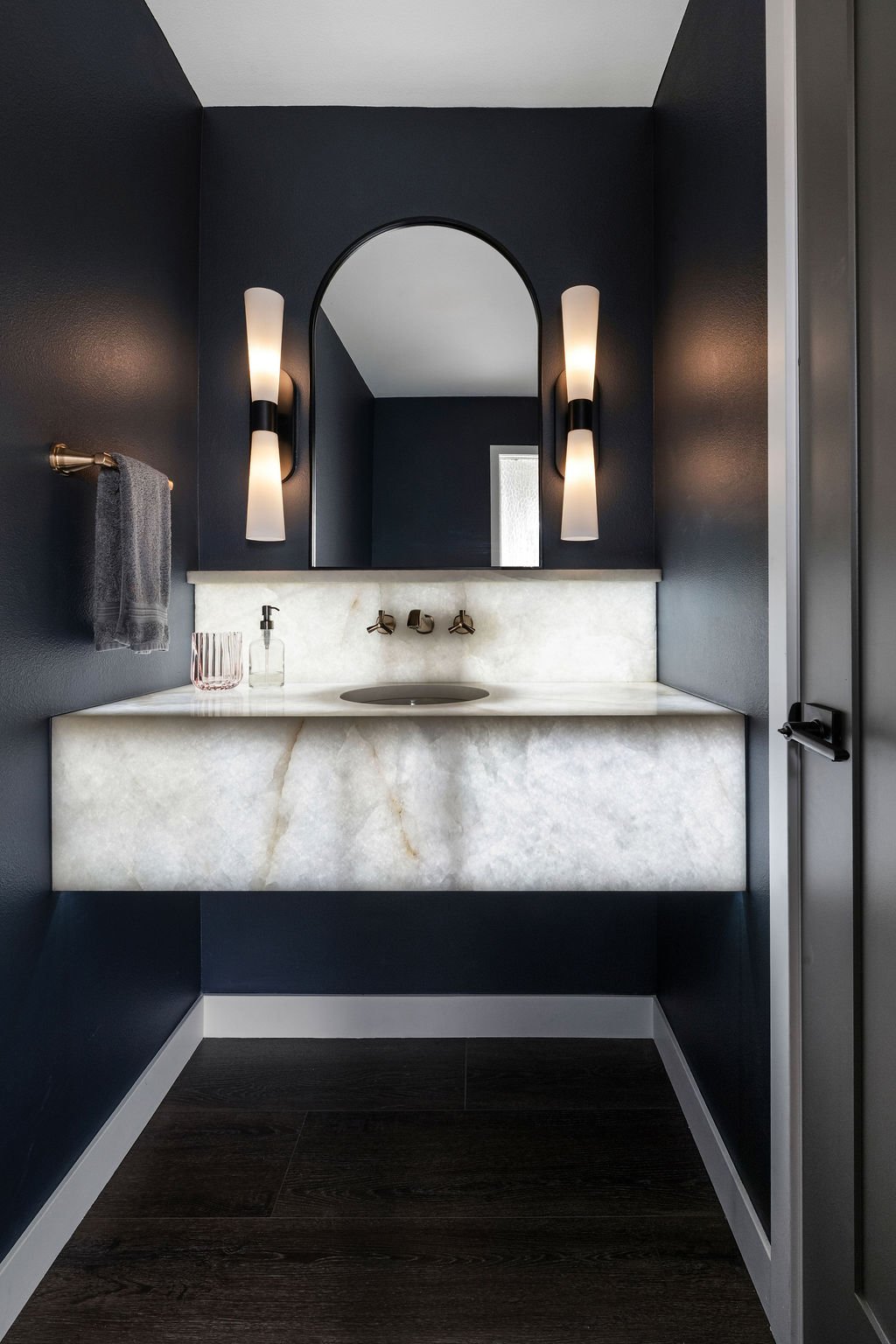 Contemporary powder bathroom with floating marble vanity, matte fixtures, and moody navy walls.