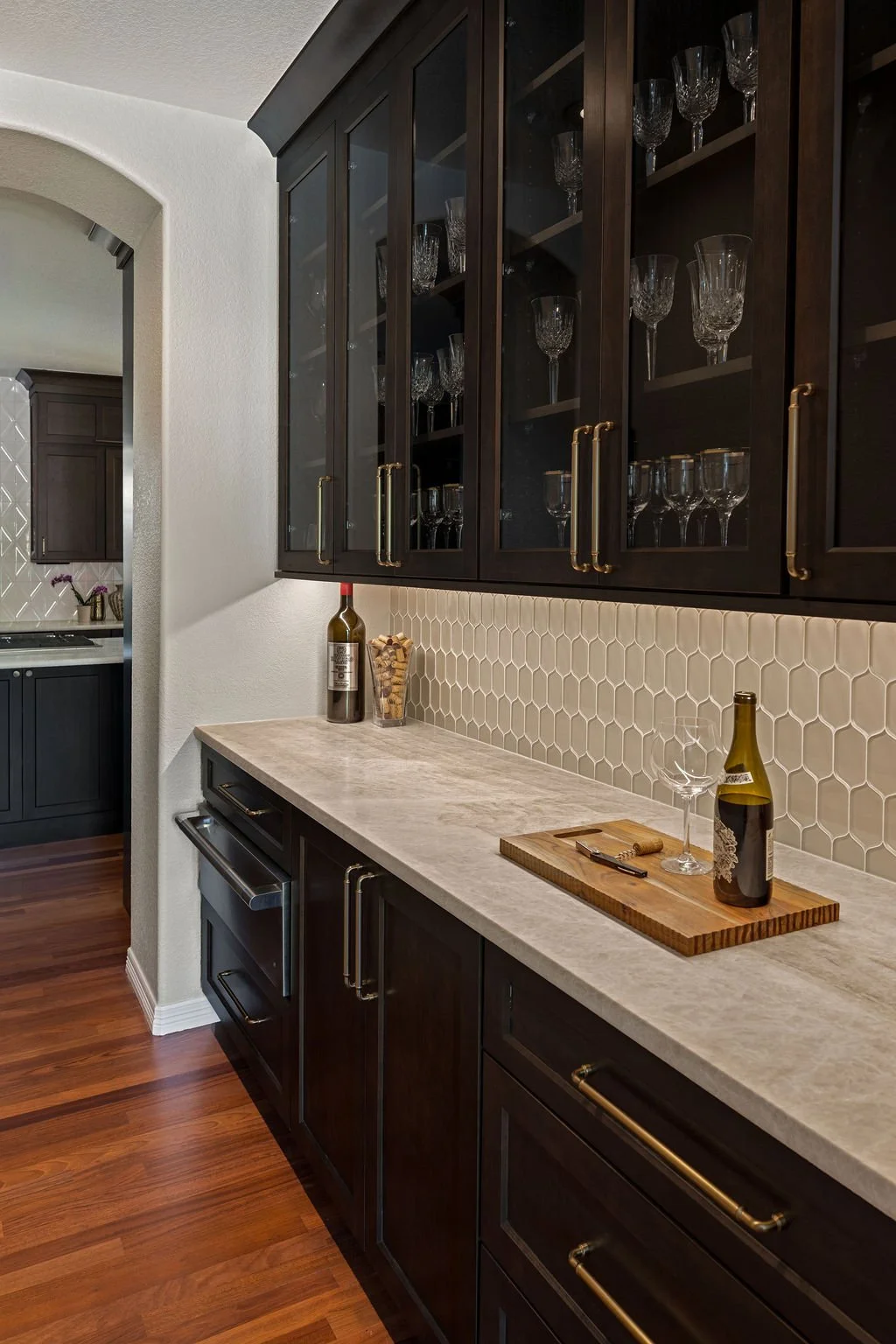 Elegant built-in wine bar with dark wood cabinetry, glass-front storage, stone countertops, and a tile backsplash.