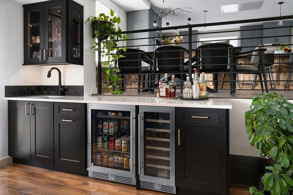 Modern home bar with black shaker cabinets, glass-front uppers, quartz countertop, and built-in beverage fridge.