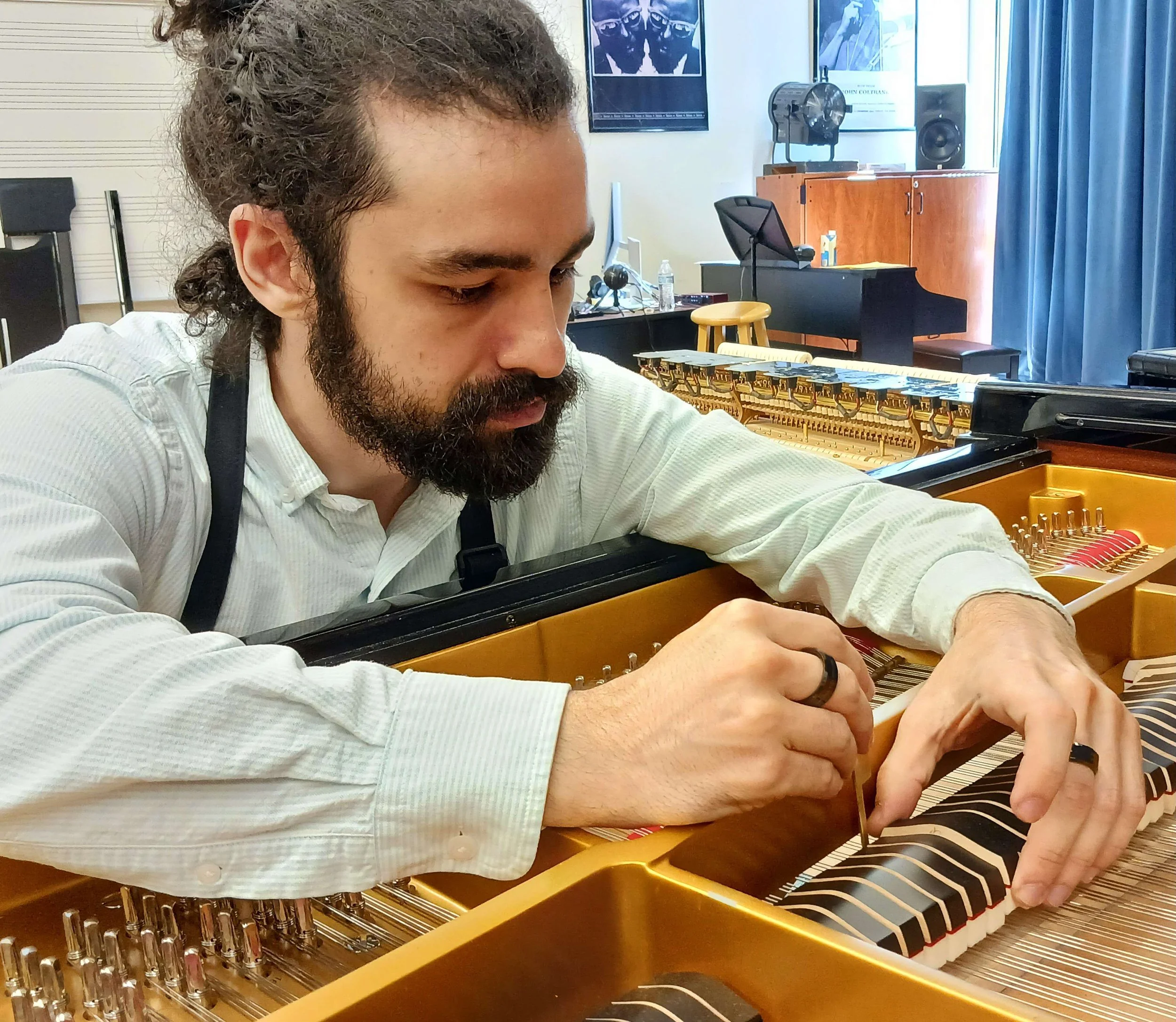 A man with a beard and long curly hair working on the inside of a grand piano in a music room.