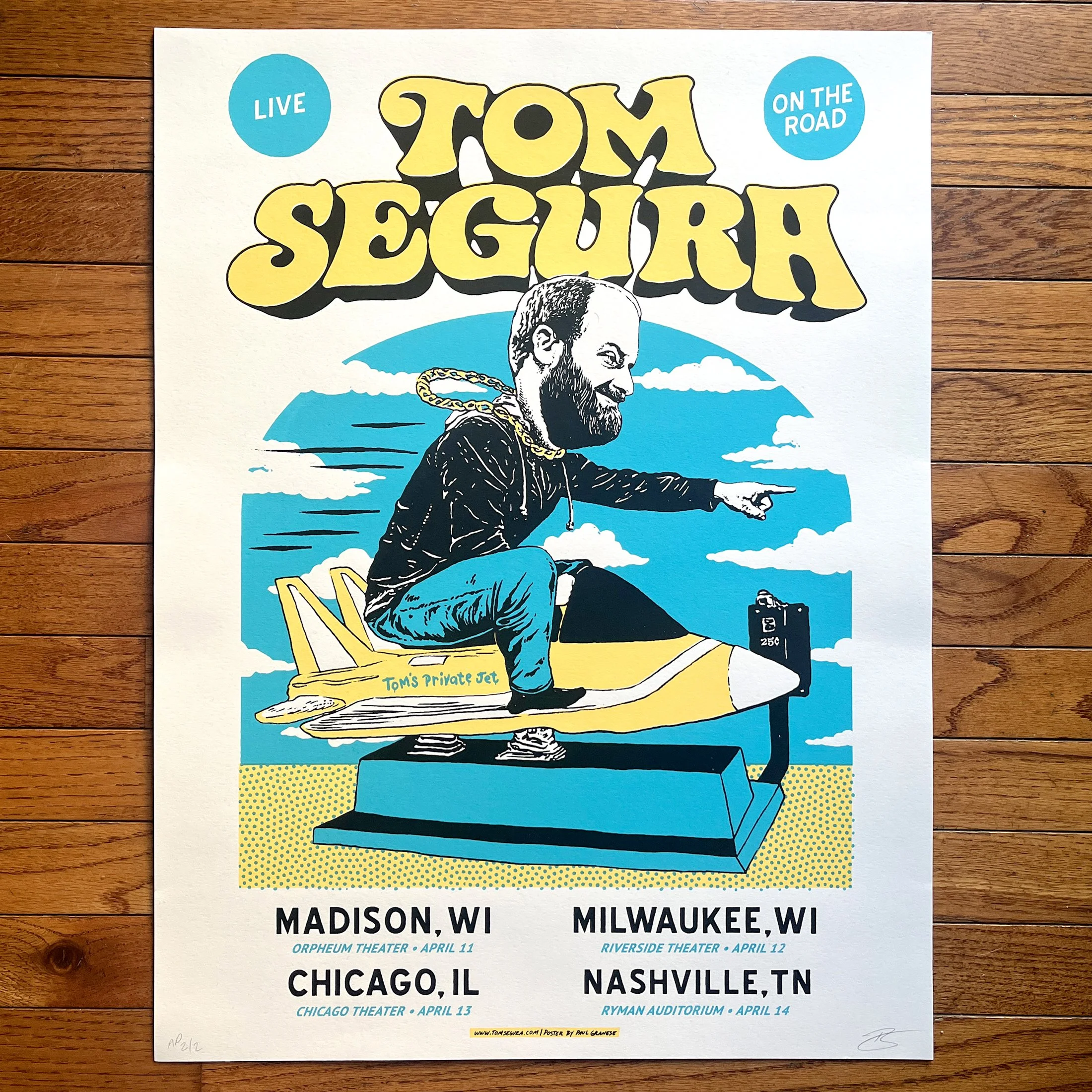 Poster advertising the 'Live on the Road Tom Segura' comedy tour with dates in Madison, WI, Milwaukee, WI, Chicago, IL, and Nashville, TN, including venue names and dates, and featuring a cartoon of Tom Segura pointing and sitting on a chair.